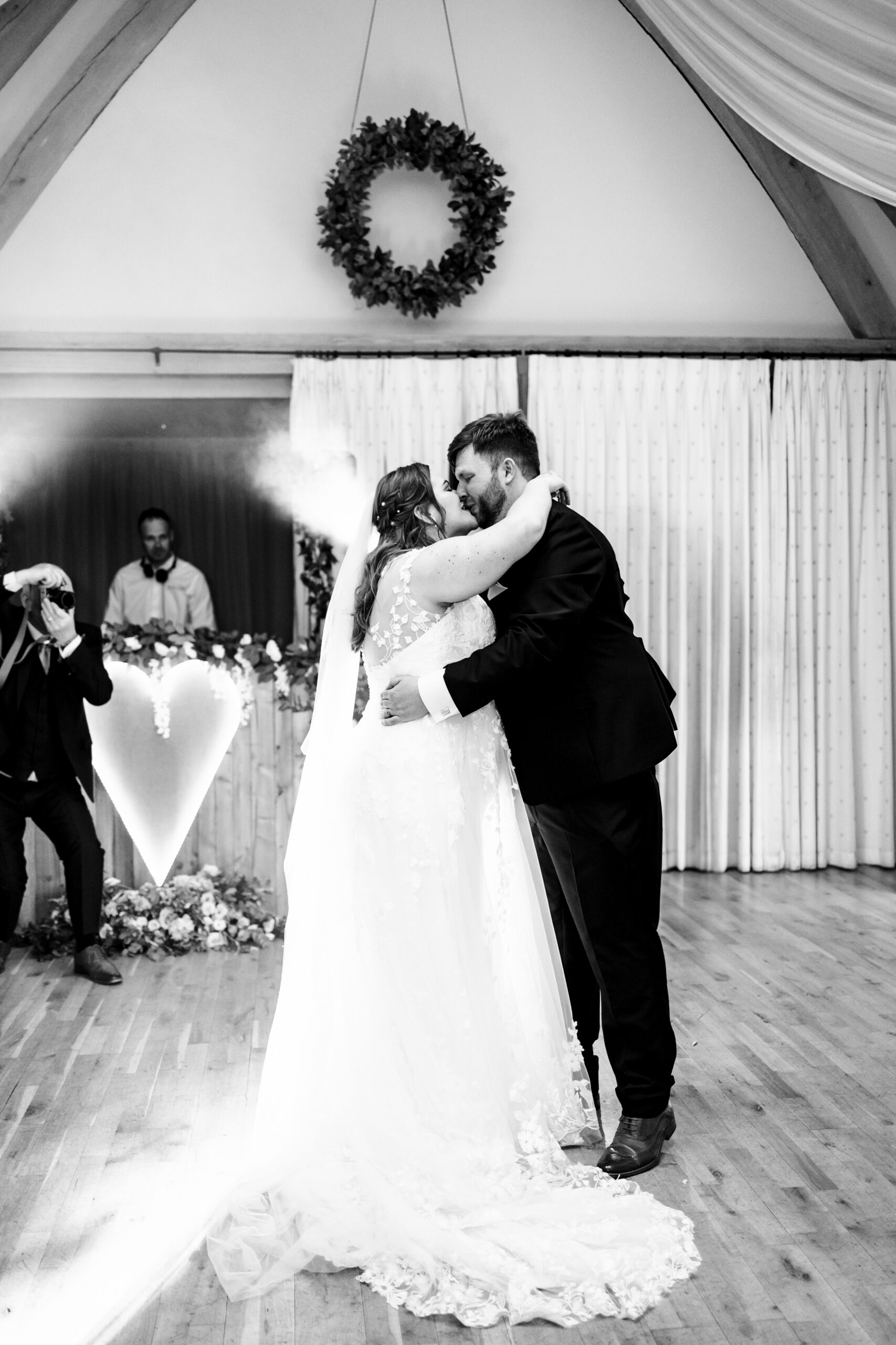 A black and white image of the bride and groom on the dance floor. They are holding each other in an embrace and are kissing. The groom has his hands around the bride's waist.