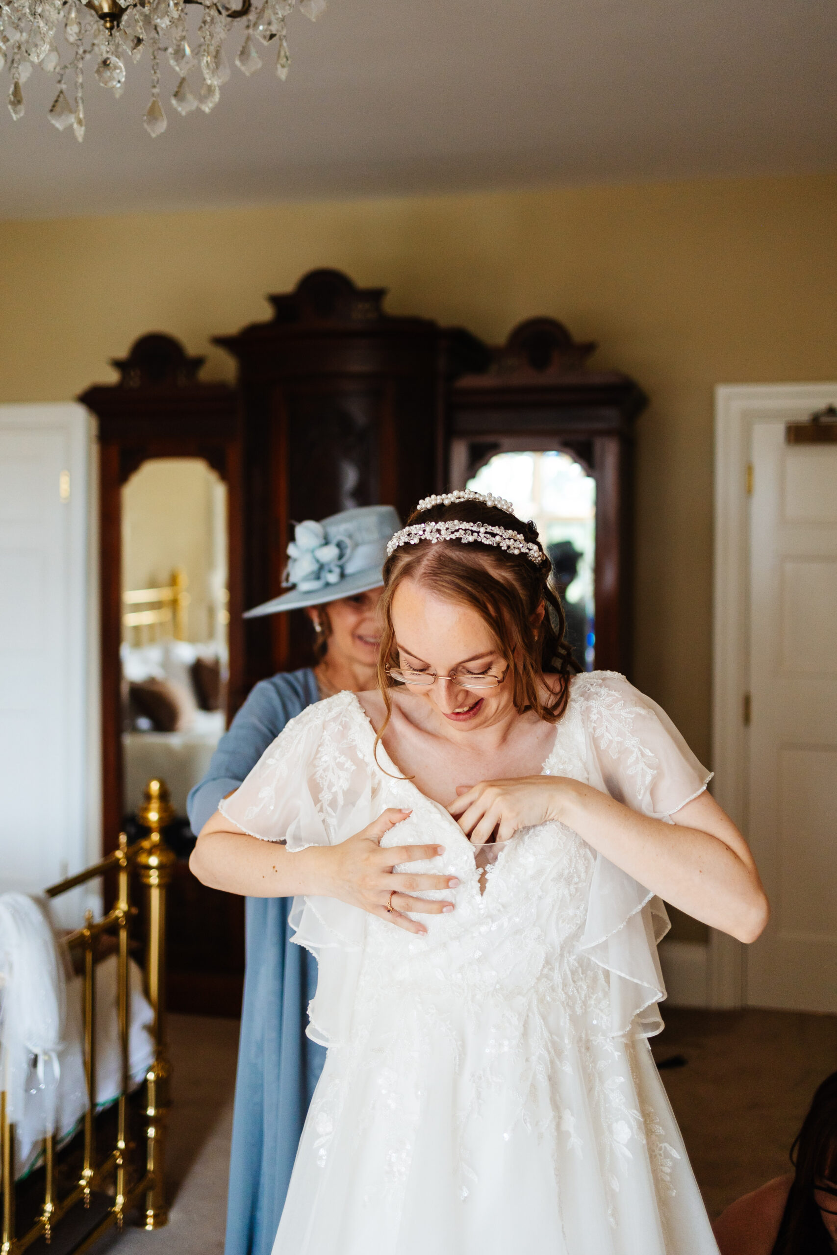 The bride getting in to her dress. Her mother is behind, helping her. They are smiling.