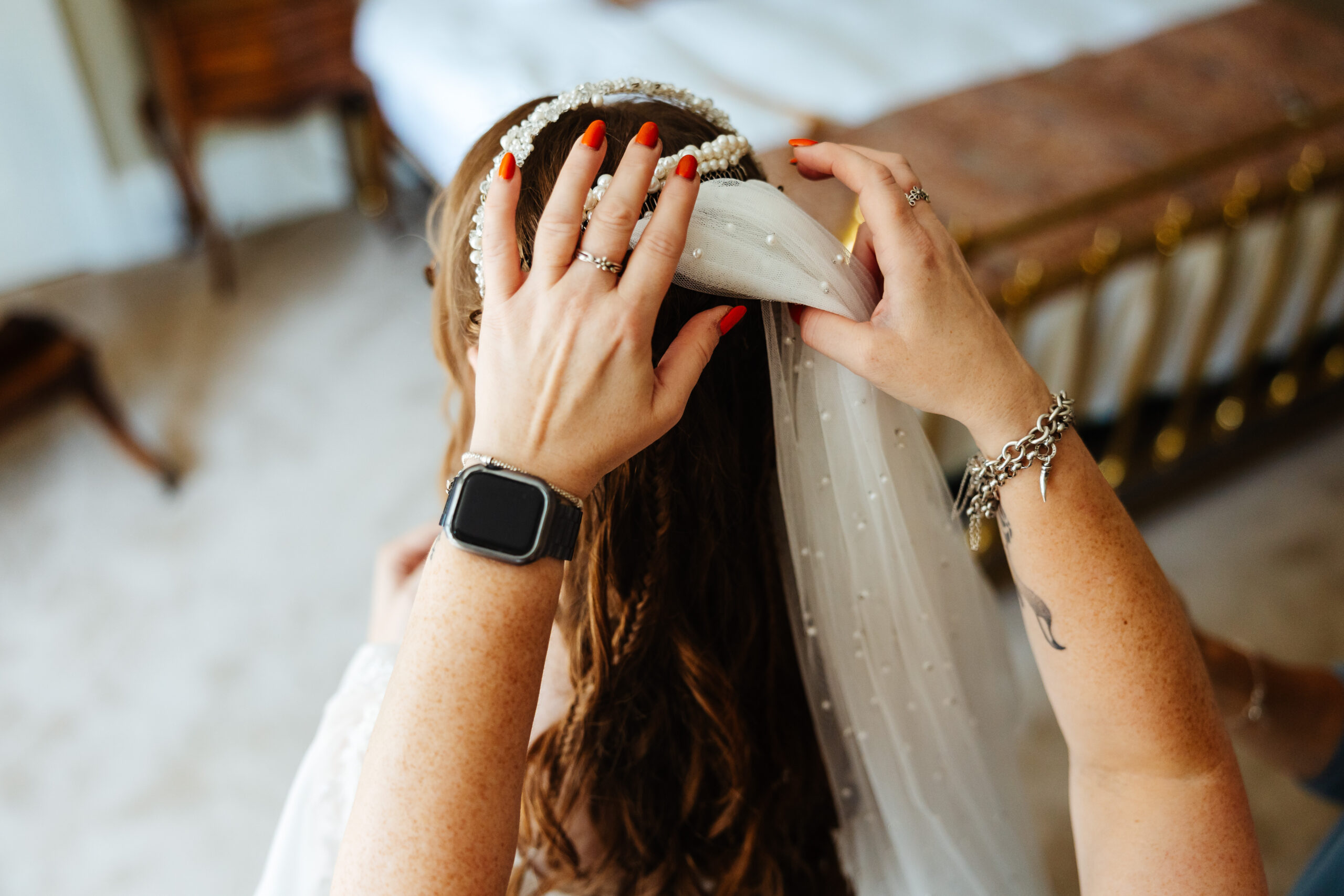 A bridesmaid helping the bride put her veil in her hair. The veil is beaded with pearls interwoven throughout.