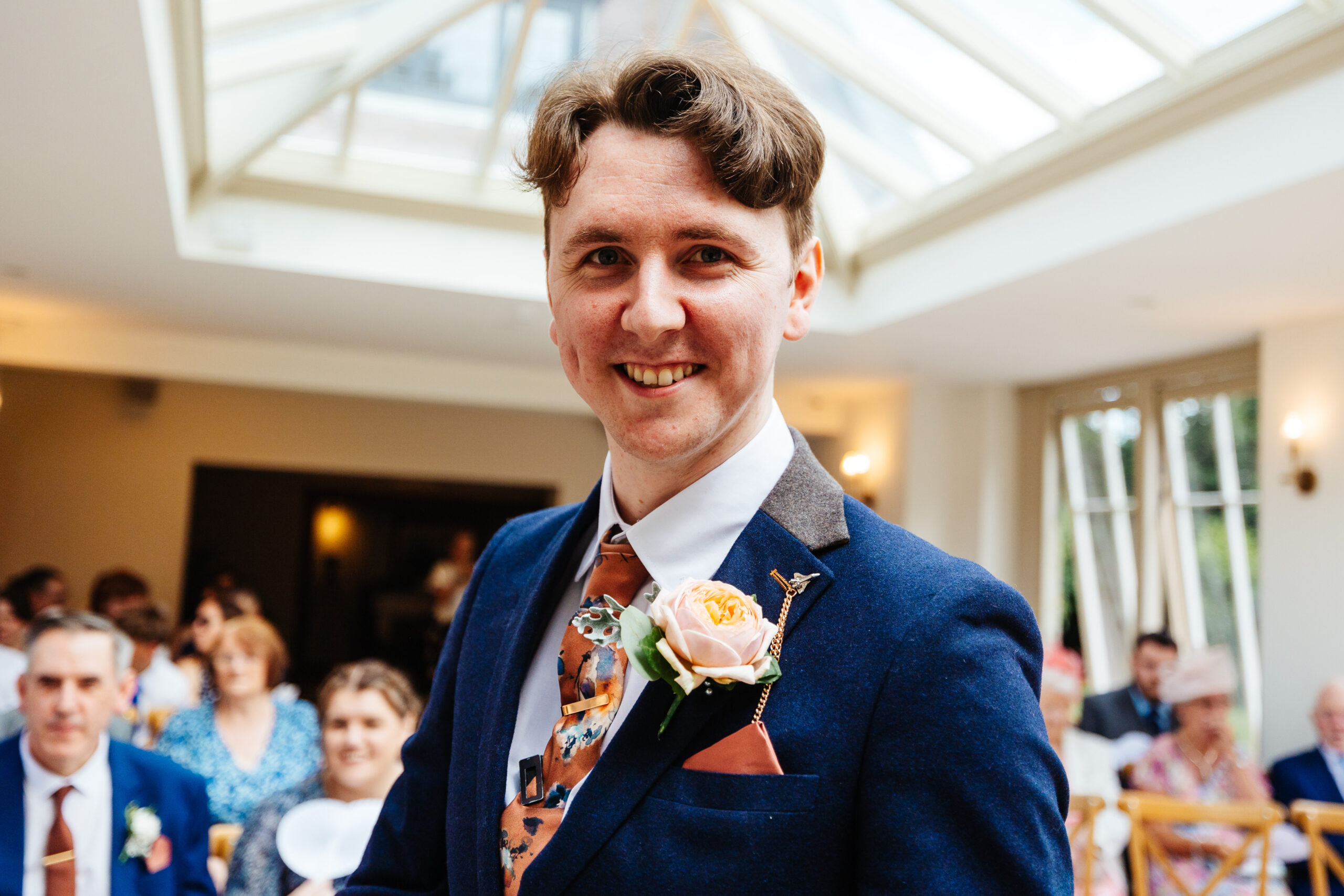 The groom at the top of the alter. He is smiling and you can see guests in the background.