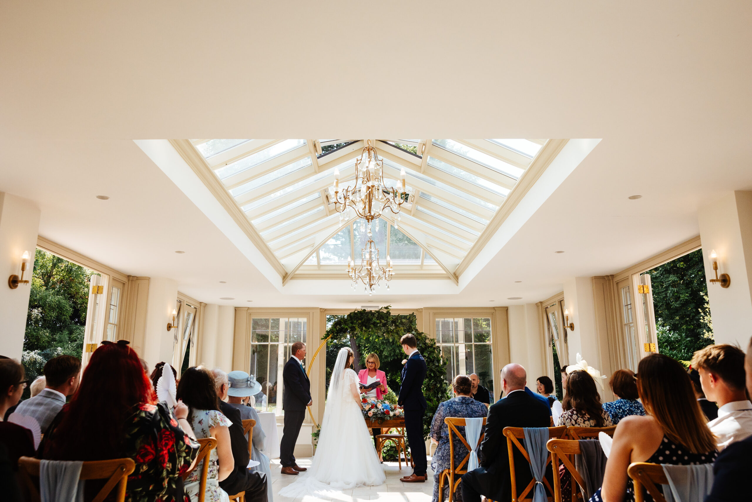 The bride and groom at the top of the aisle. The celebrant is in the middle reading from a book. The bride's father is to the side of the bride.