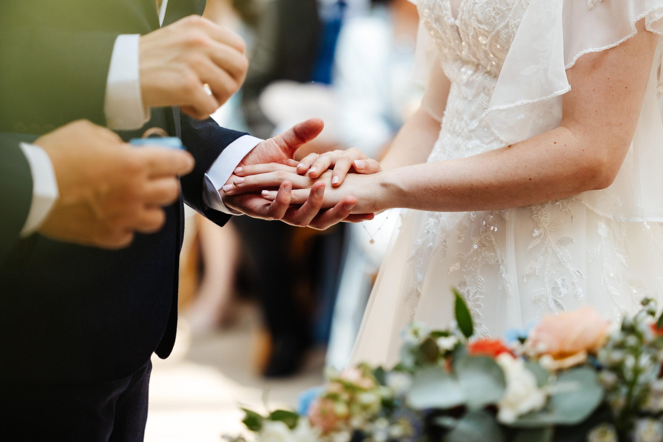 The bride and groom's hands. The groom is putting a ring on the brides hand. The bride has beautiful pale pink nails.