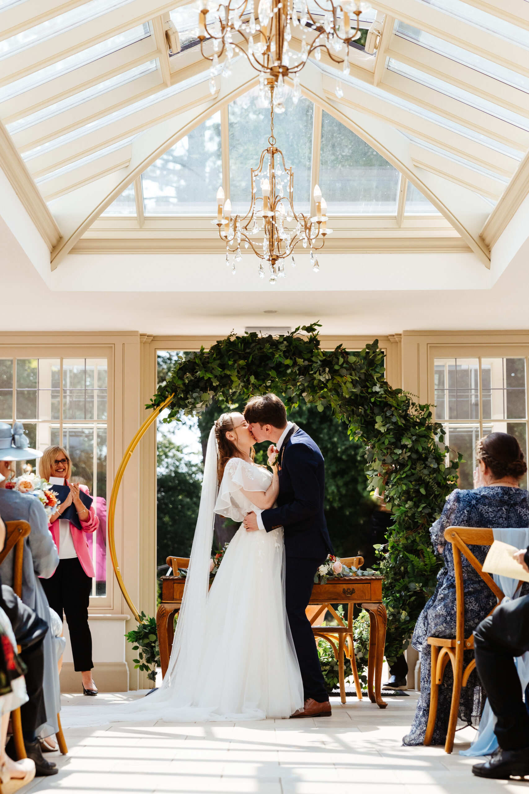 The bride and groom at the top of the alter. They are kissing. Everyone around them looks happy and they are clapping.