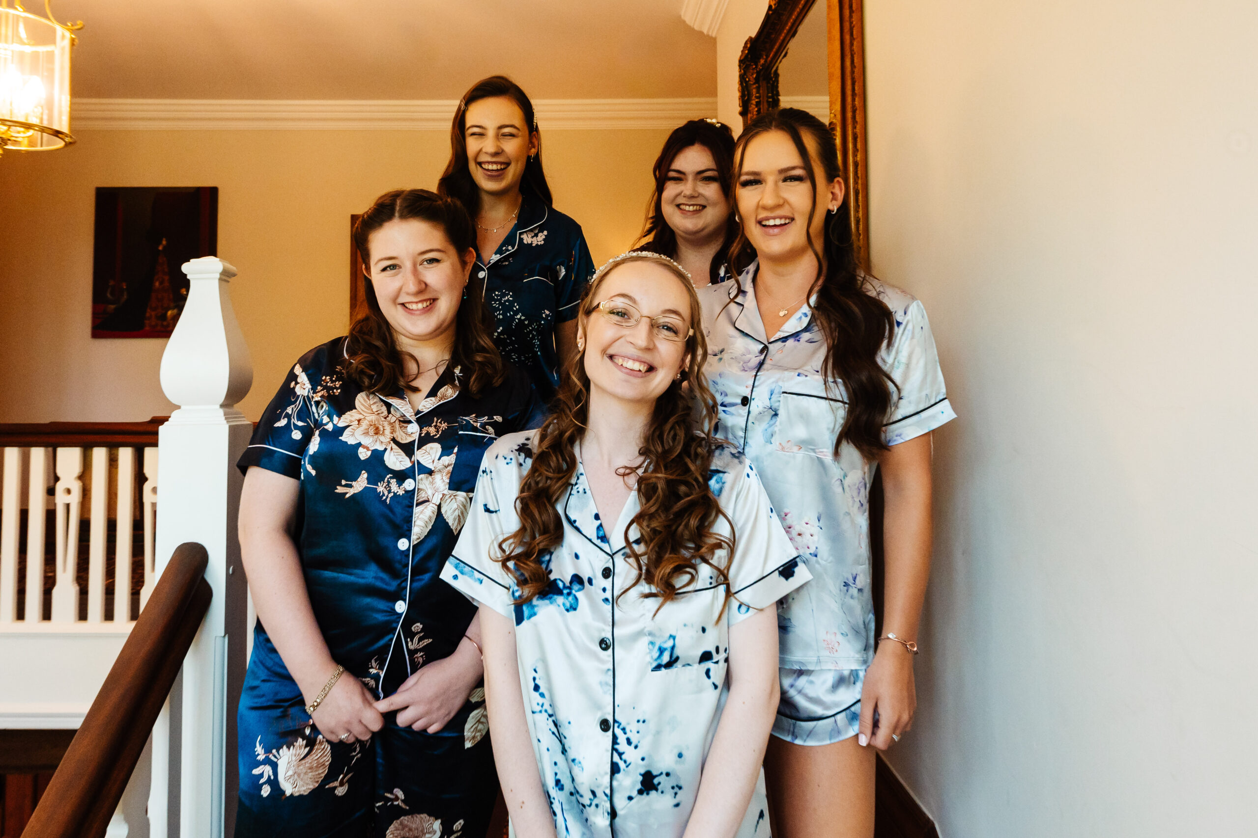 The bride and her bridesmaids. They are in silk pyjamas which have a floral pattern on. They are all smiling.