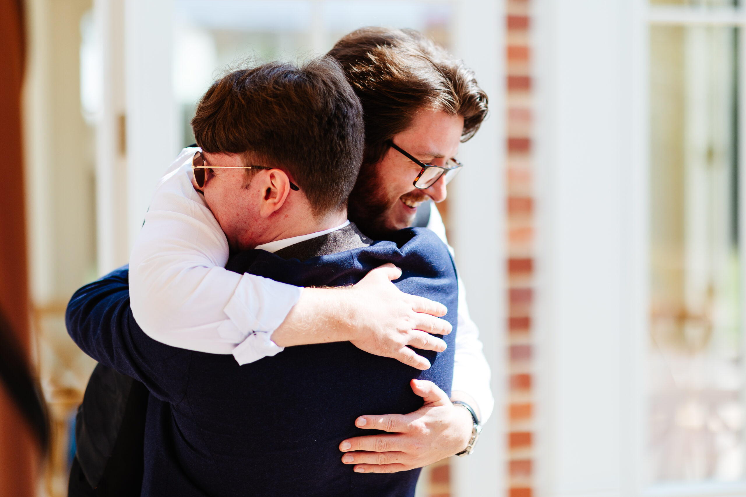 The groom and a guest hugging. They are both smiling.