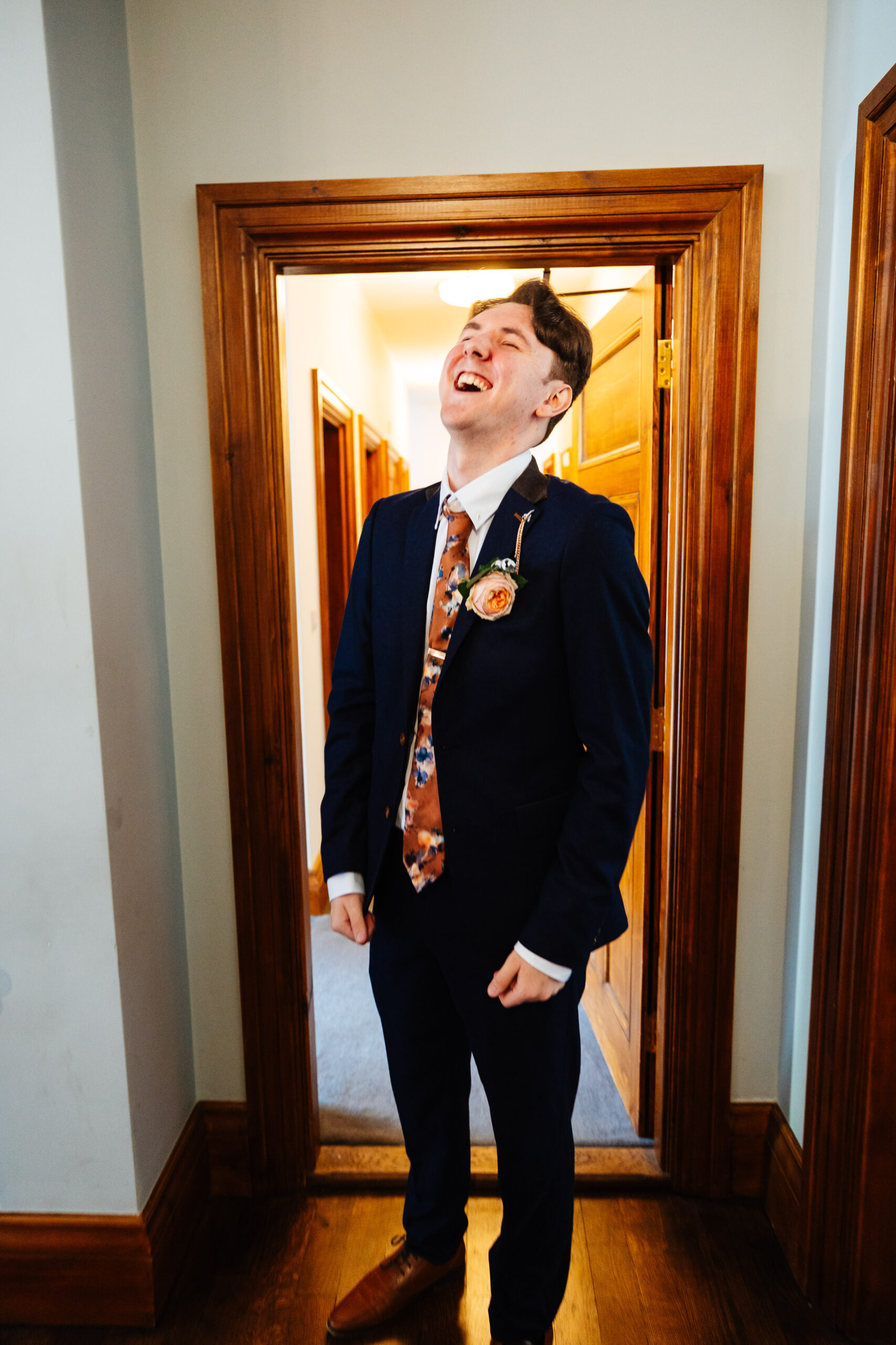 The groom in his navy suit looking up to the sky and smiling and laughing. 