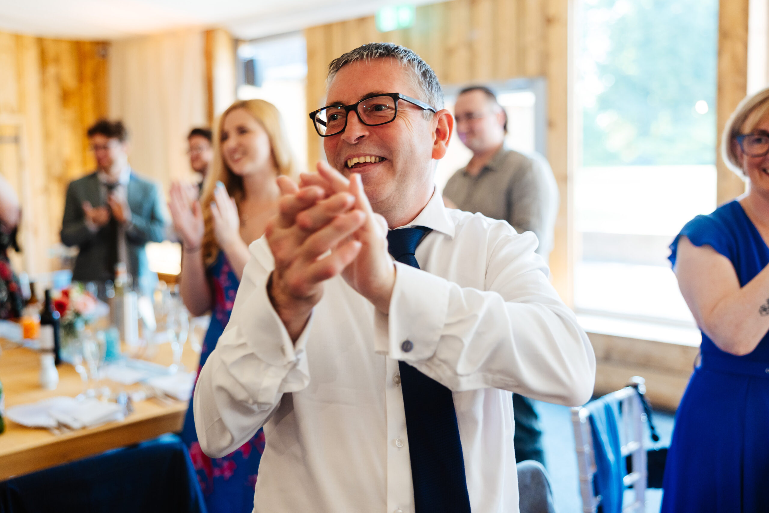 A guest looking at the couple as they enter the breakfast. He is smiling at them and clapping his hand.