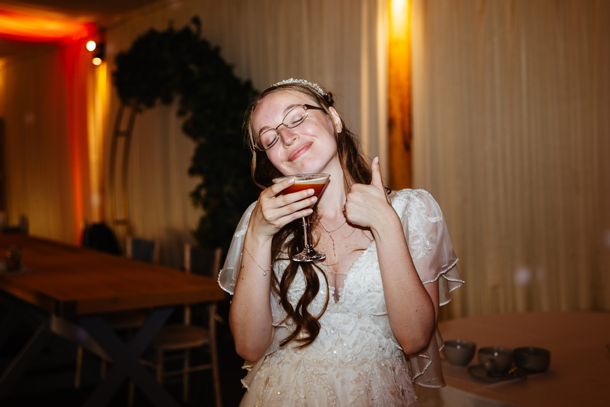 The bride drinking a coktail. She is closing her eyes and smiling and has her thumb up.