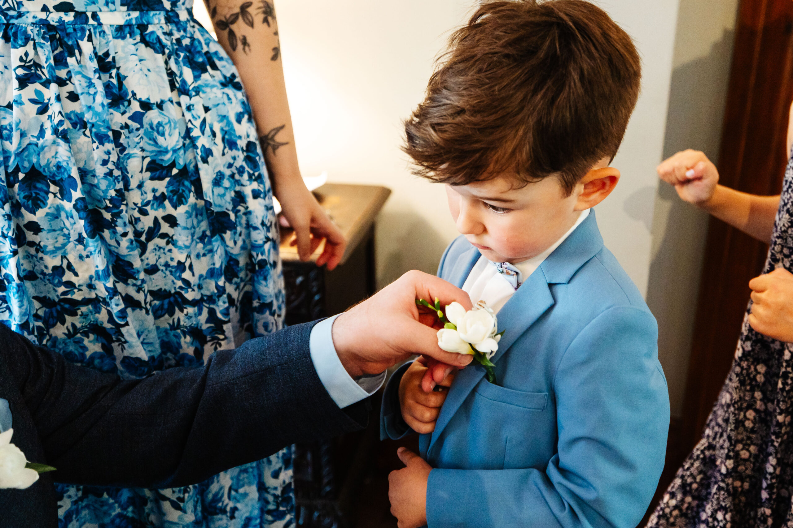 A little boy in a pale blue suit. He looks very smart and is wearing little white flowers in his buttonhole.