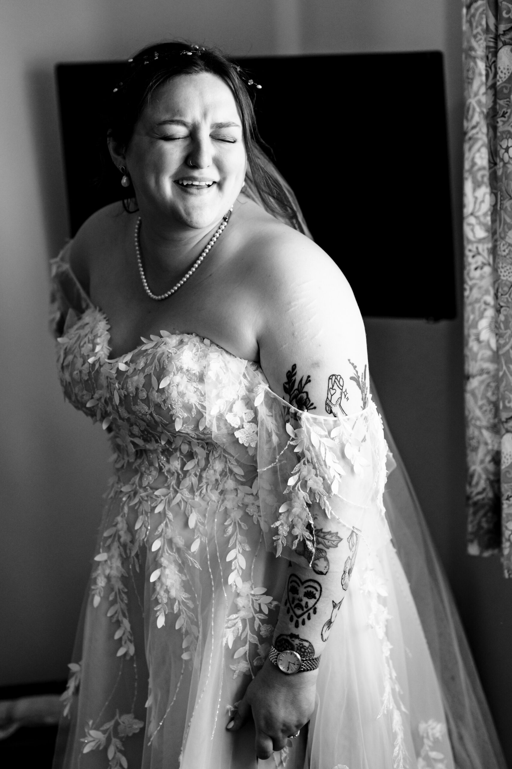 The bride in her dress. It is a strapless dress with a lace detail on it. She has her eyes closed and is smiling.