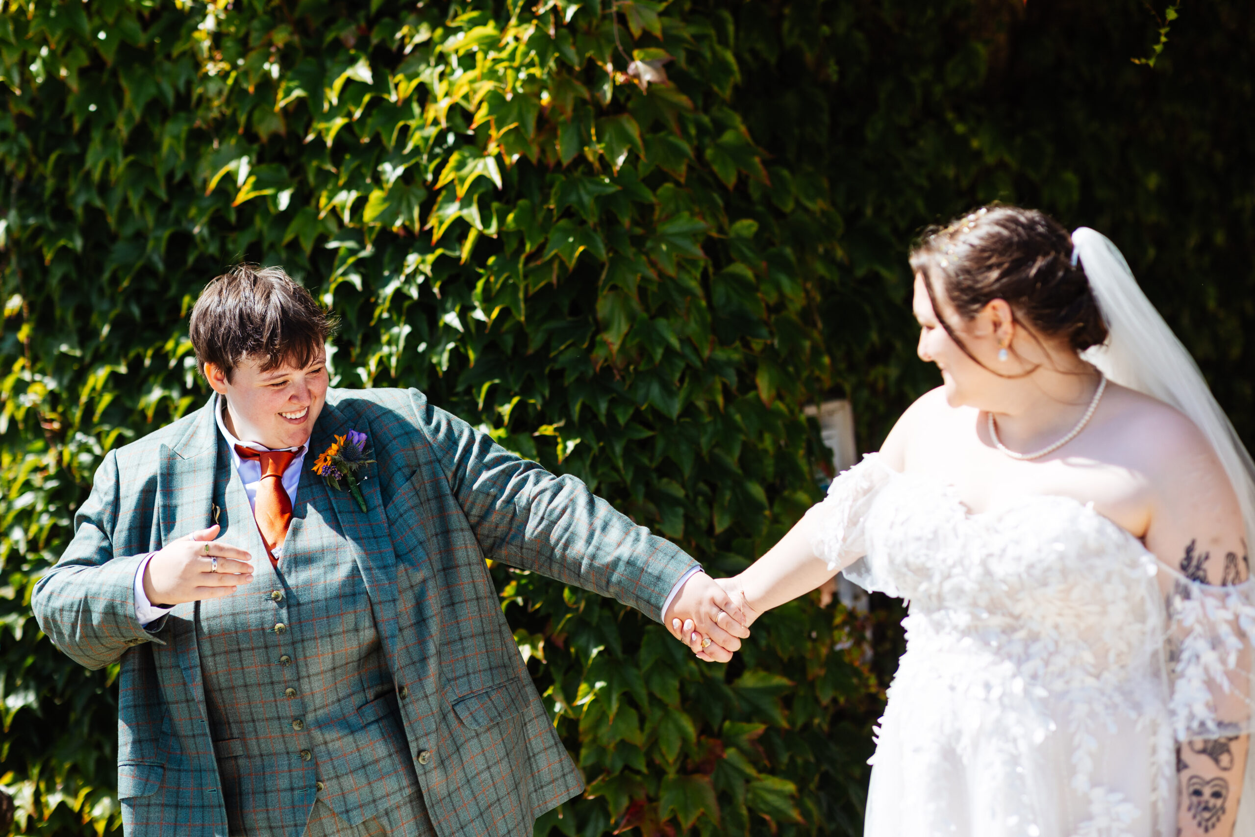 The brides seeing each other for the first time. They are looking at each other and smiling. They are holding hands.