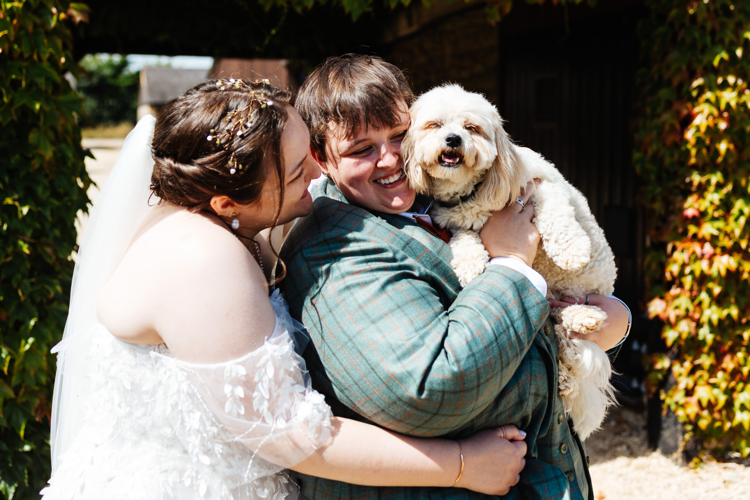 A photo of the brides and their dog. They are holding their dog and hugging each other.