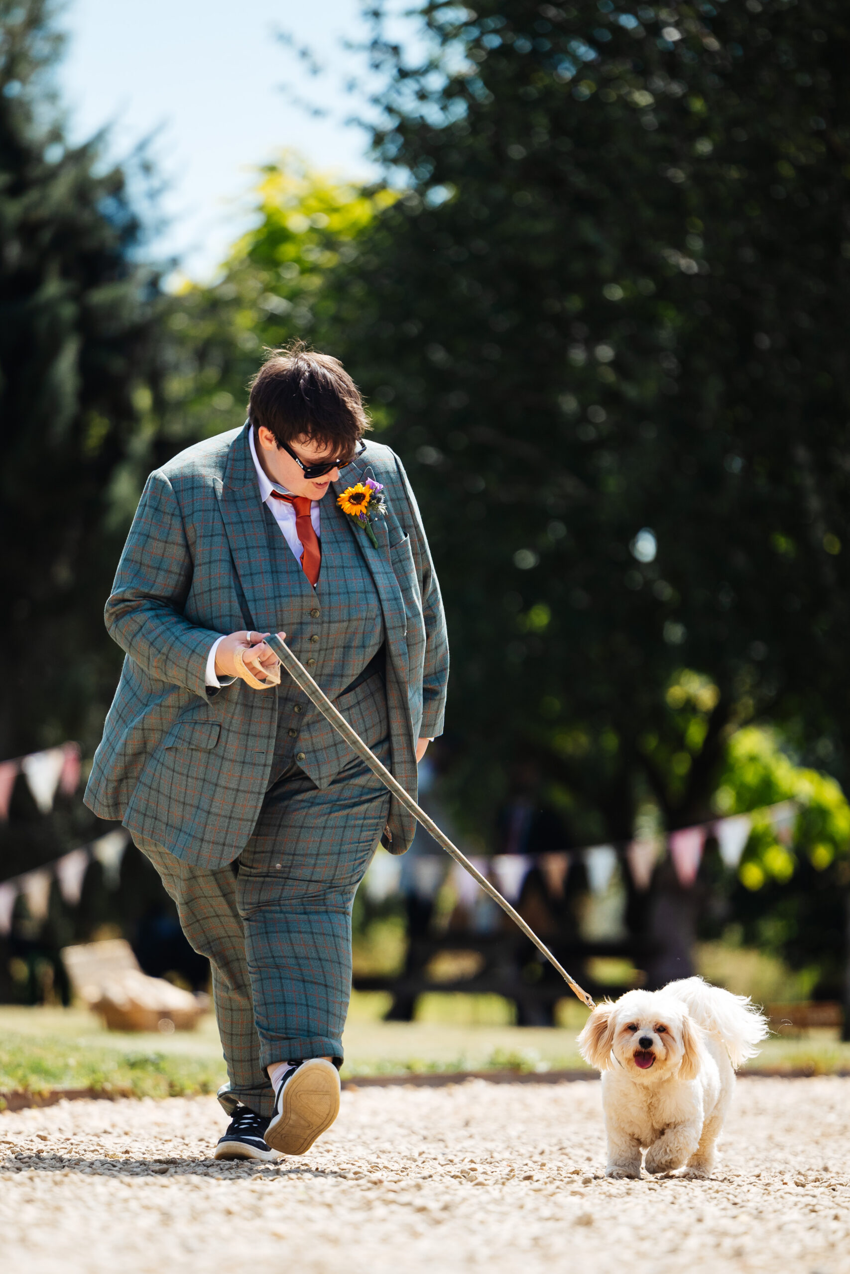 A photo of one of the brides and her dog. Her dog is on a lead and the lead matches the bride's suit pattern.