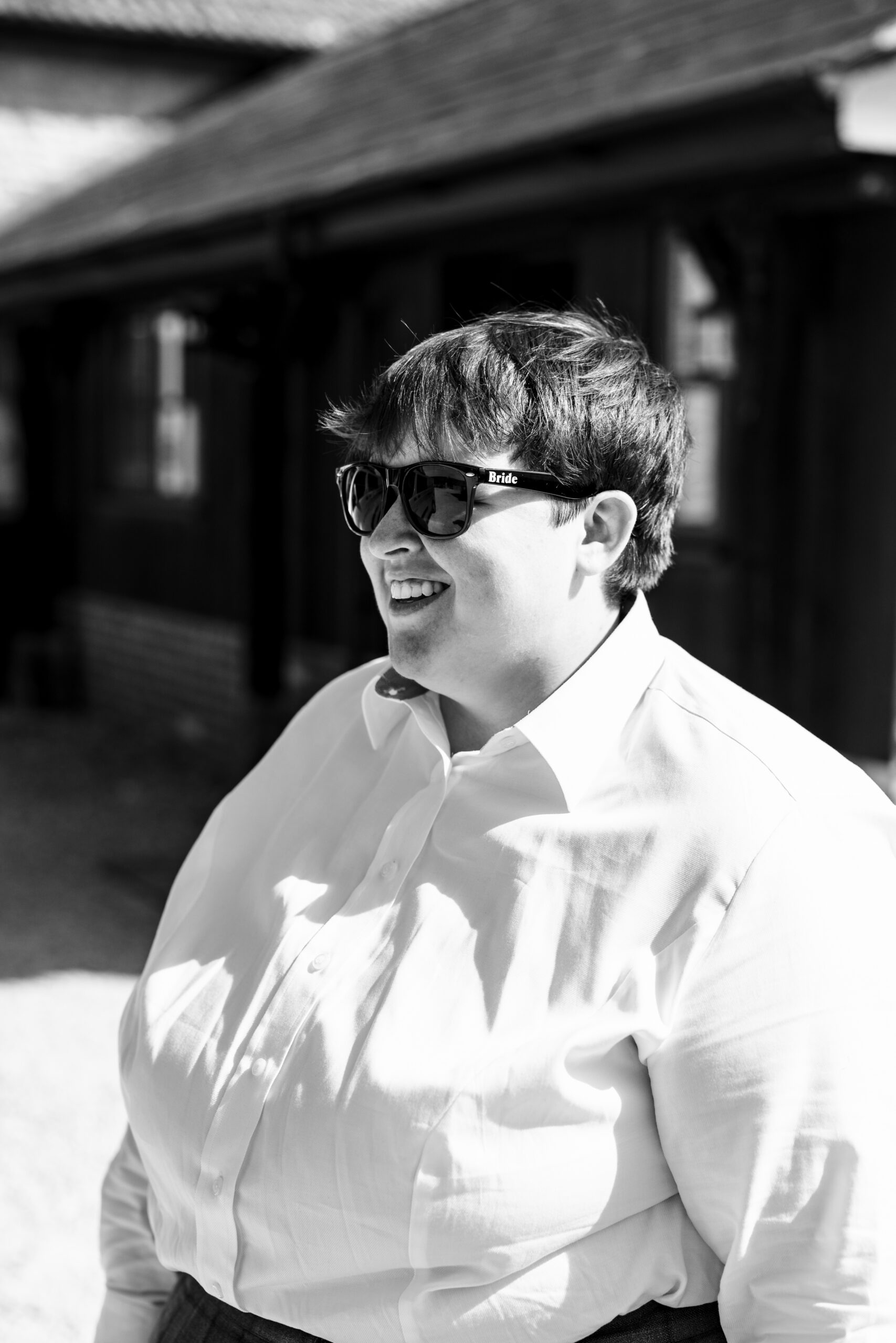 A black and white image of the bride. She is wearing a white shirt and black sunglasses with the word bride written on the arm of the sunglasses.