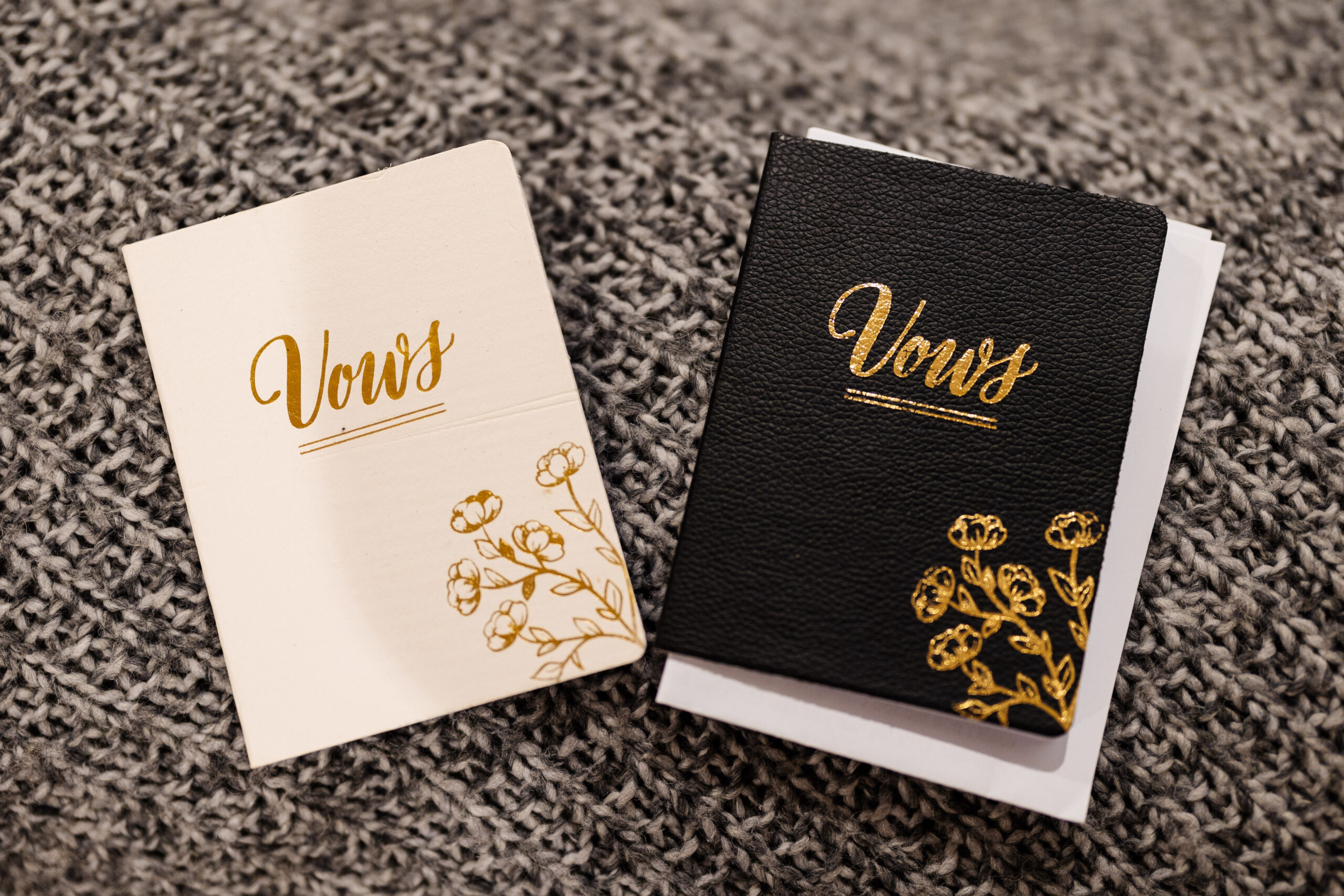 Two leather bound books with the word vows on them. One is white and the other black and both have gold detailing on them.