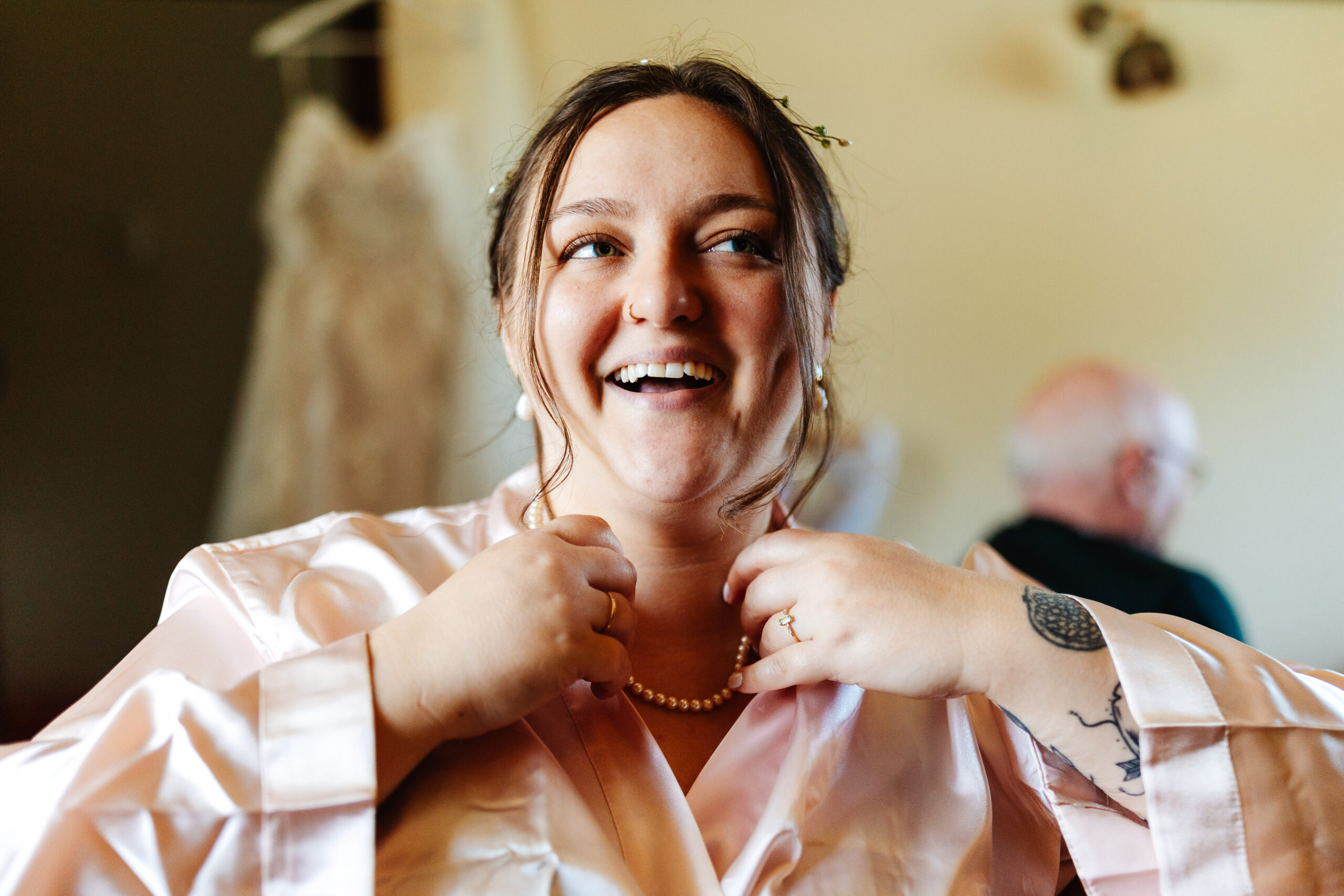 A picture of the bride getting ready. She is wearing a blush pink, silk dressing gown.