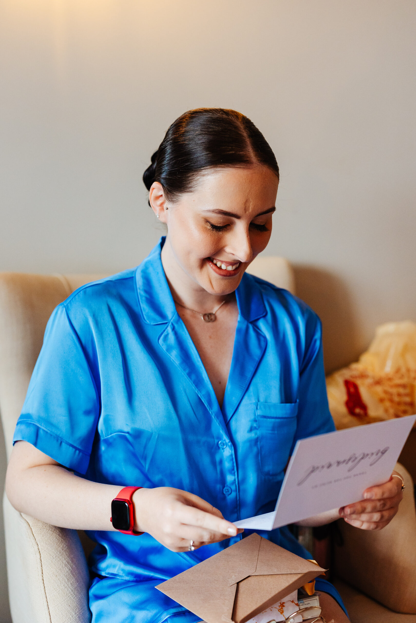 A bridesmaid wearing power blue pyjamas. She is looking at a card that says Bridesmaid on and she is looking down, reading it and smling.