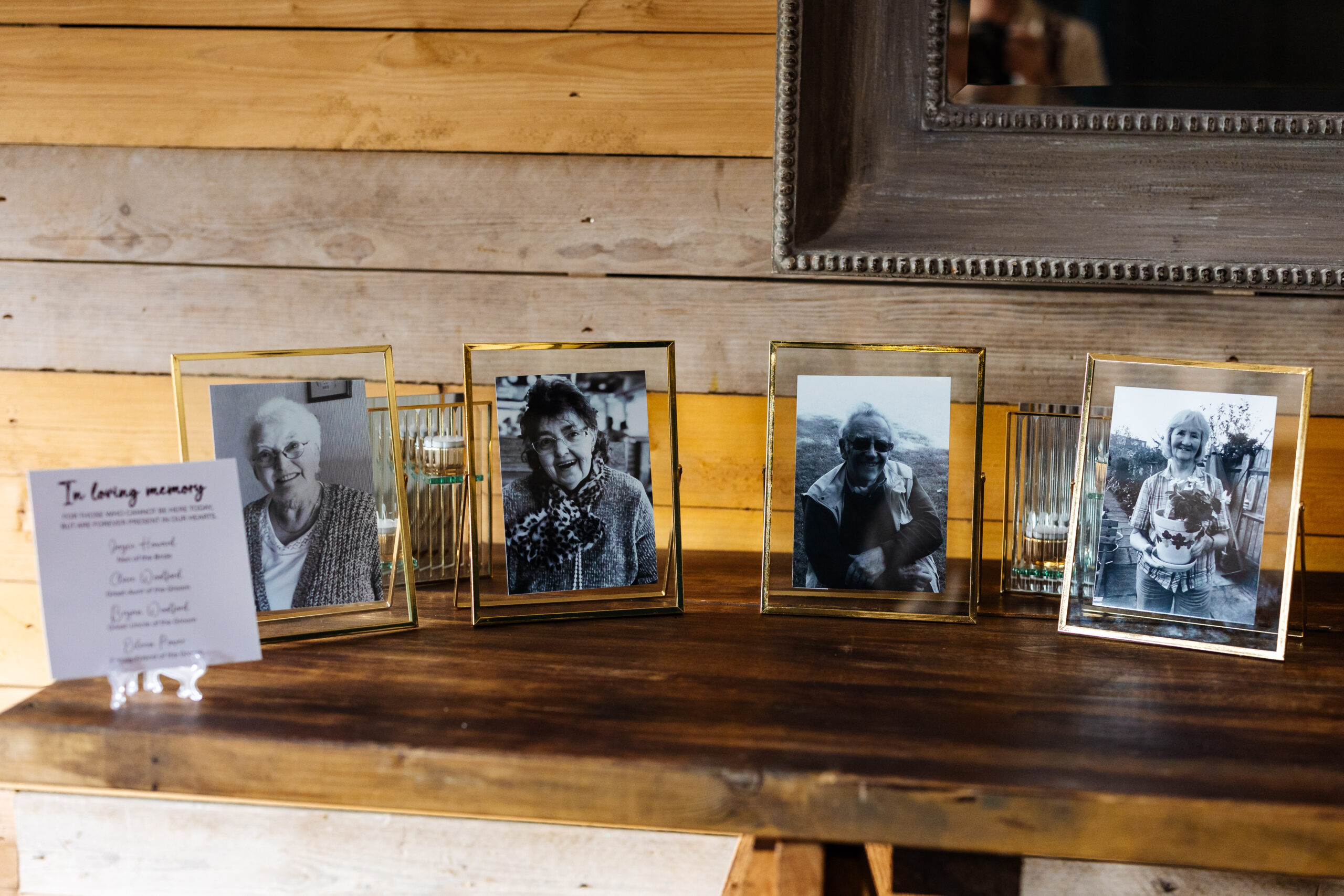 Four photo frames of black and white images. They are of older people who the couple have sadly lost. They are in gold frames and there is a sign in front that says in loving memory.