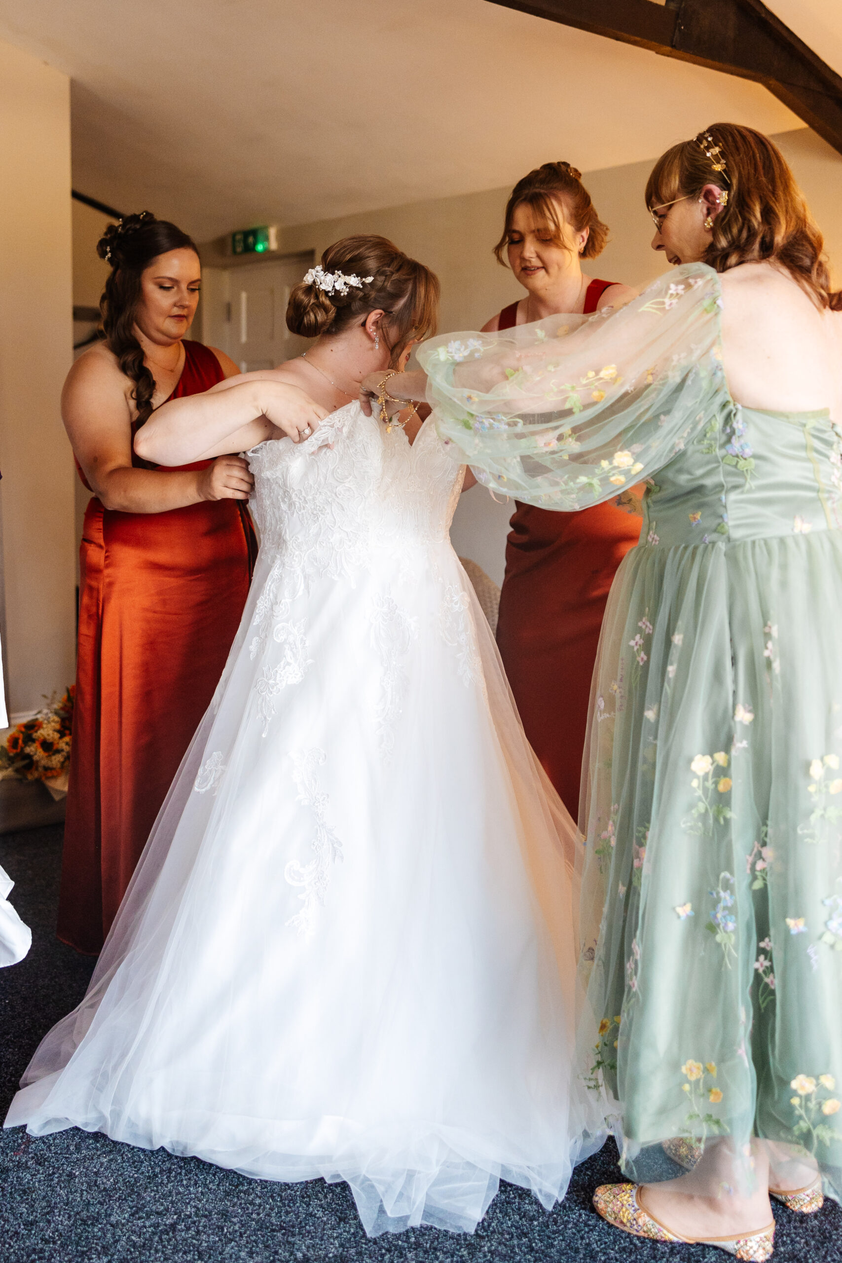 The bride getting in to her wedding dress. There are three other women helping her in to it, with hands on the dress and the bride herself.