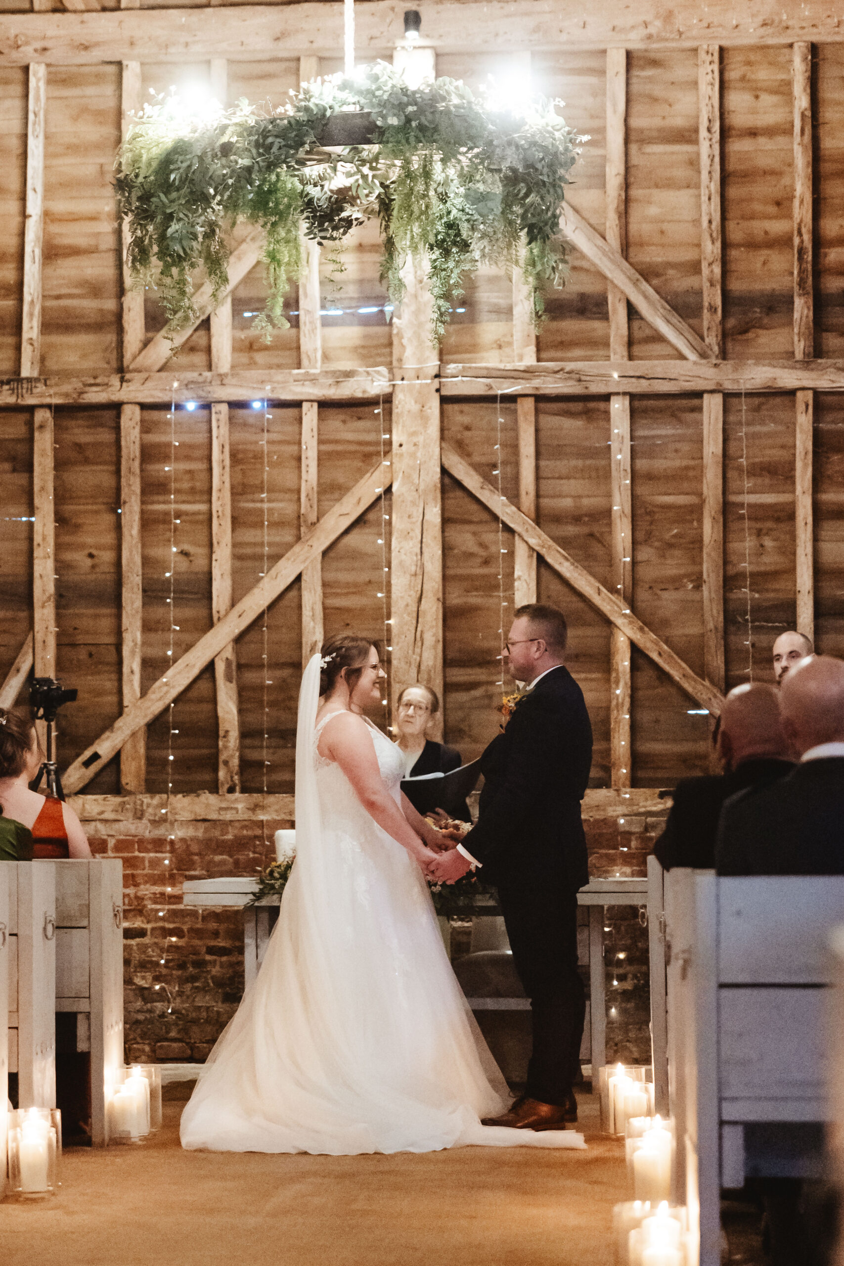 The bride and groom at the top of the alter. You can see the celebrant in the middle of them. They are smiling at each other and holding hands.