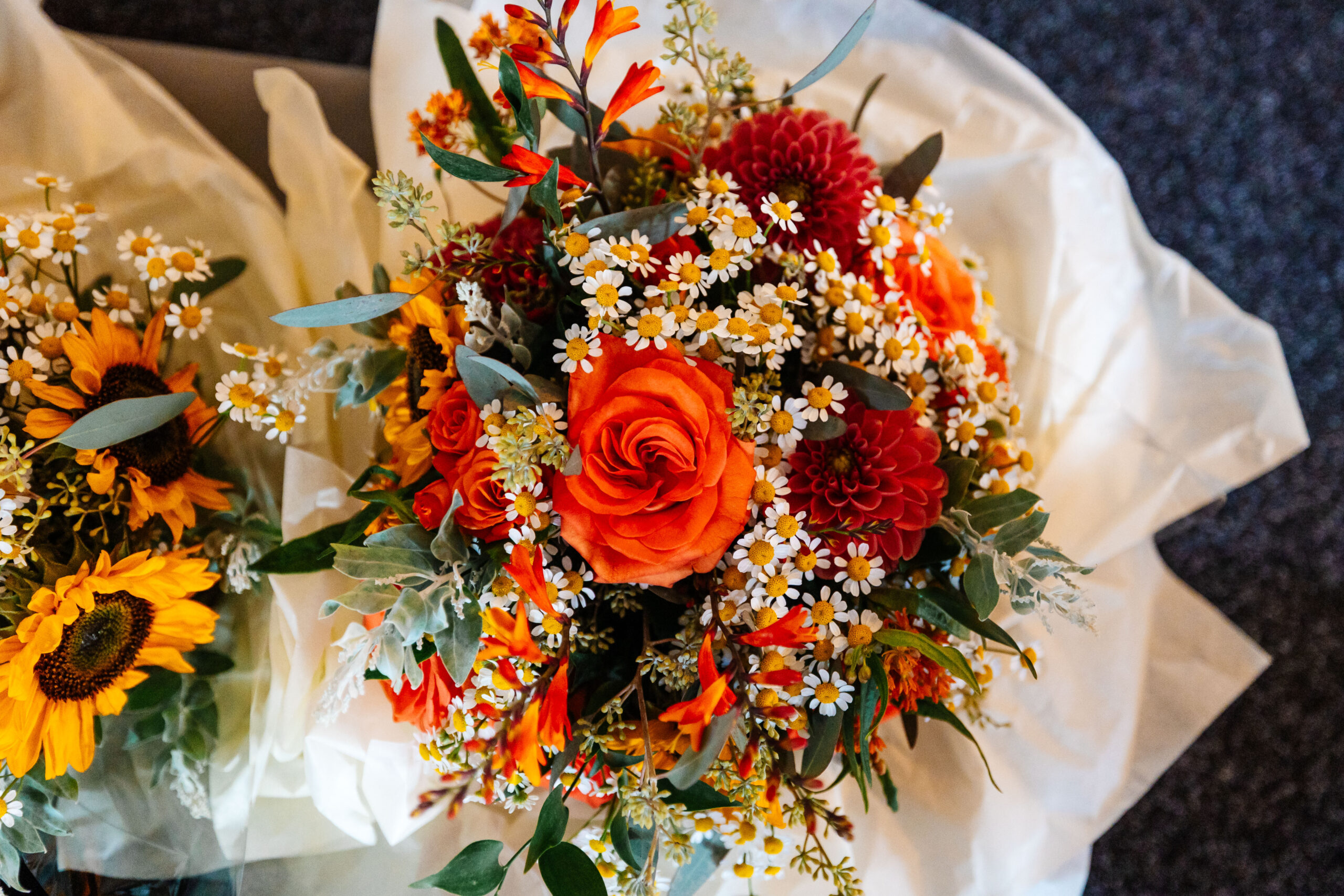 A big bunch of flowers. There are orange roses and dahlias in there and between them are scattered, wild daisies.