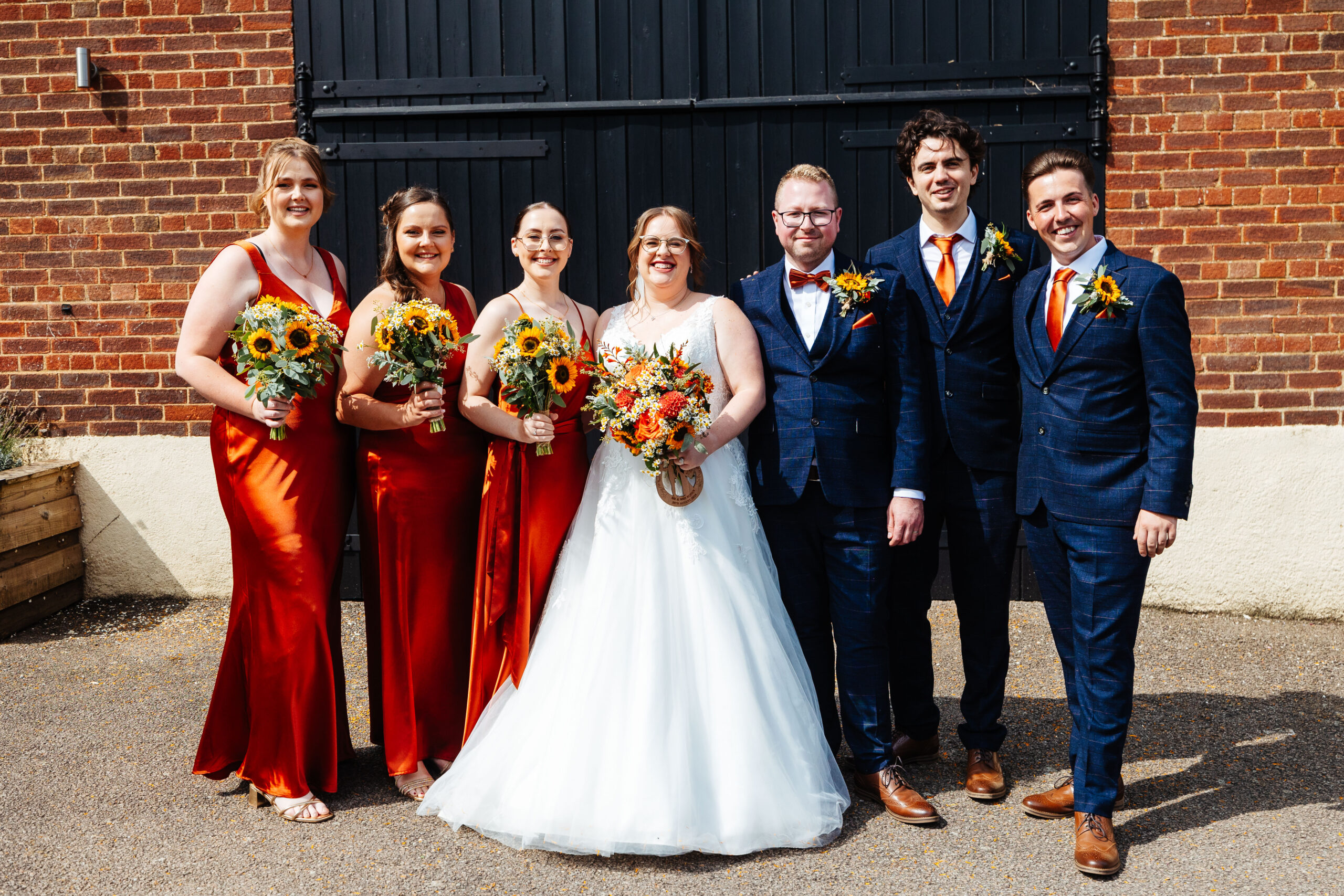 A group shot of the bridal squad; bridesmaids and groomsmen. They are looking at the camera and smiling and the bride and groom are in the middle.