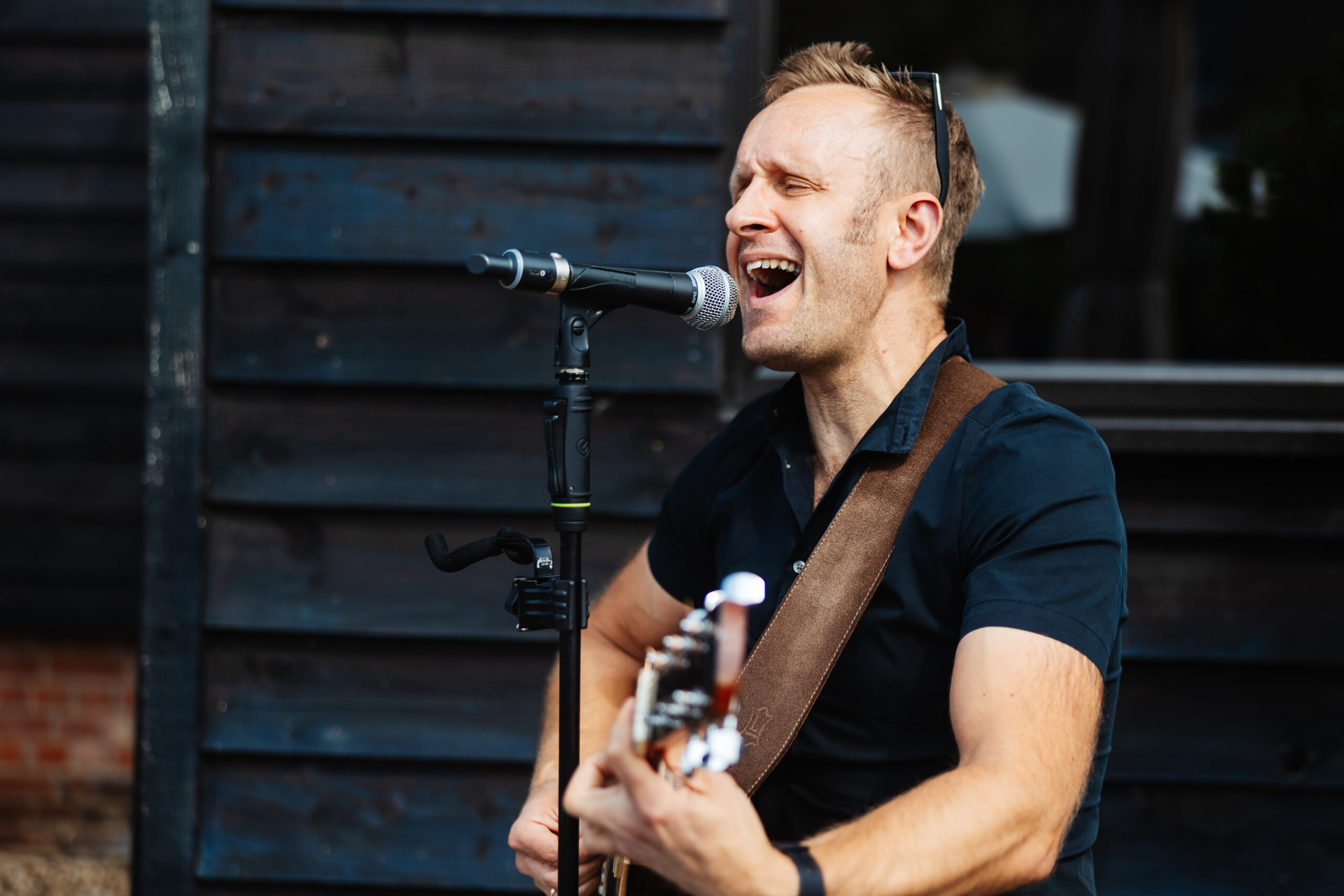 A musician singing in to a microphone and playing a guitar.