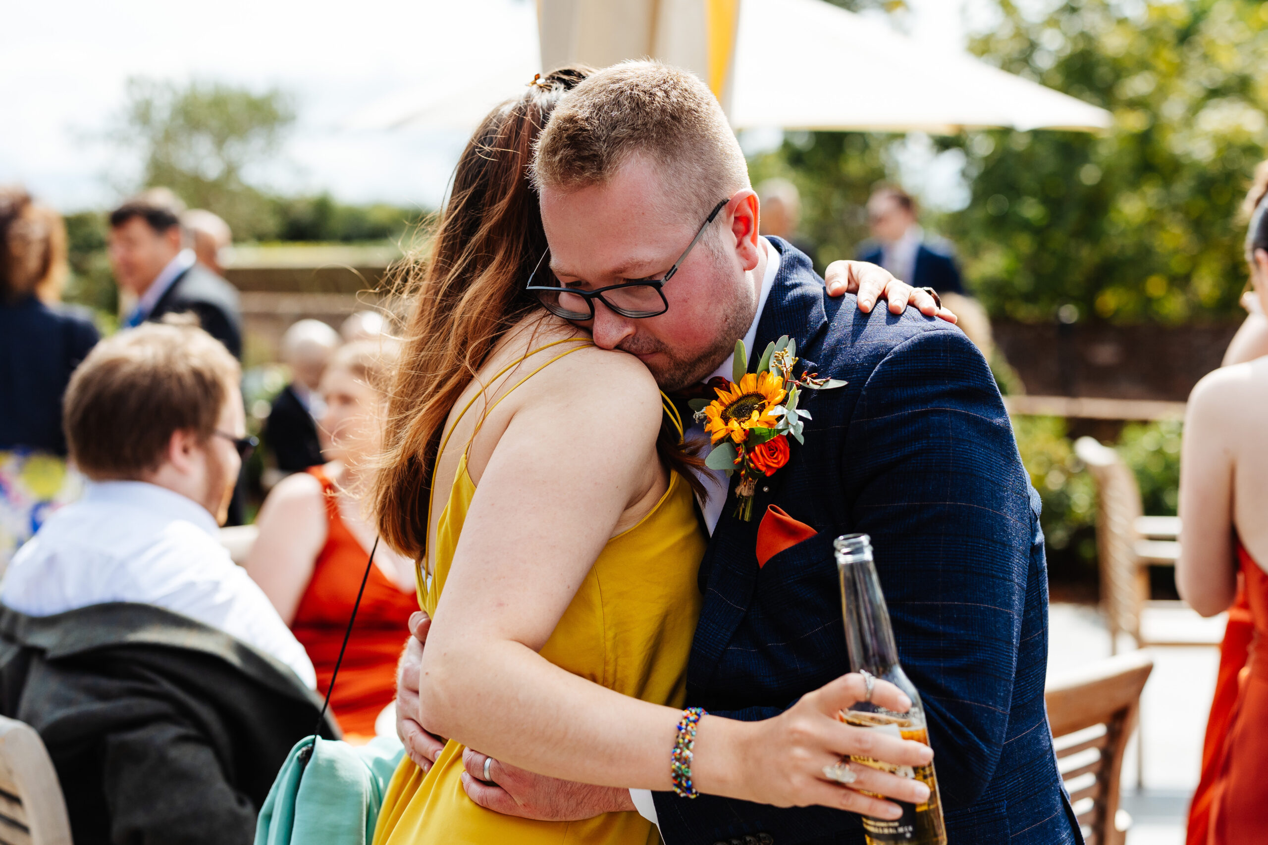 The groom hugging a female guest. She is in a yellow dress and is holding a beer.