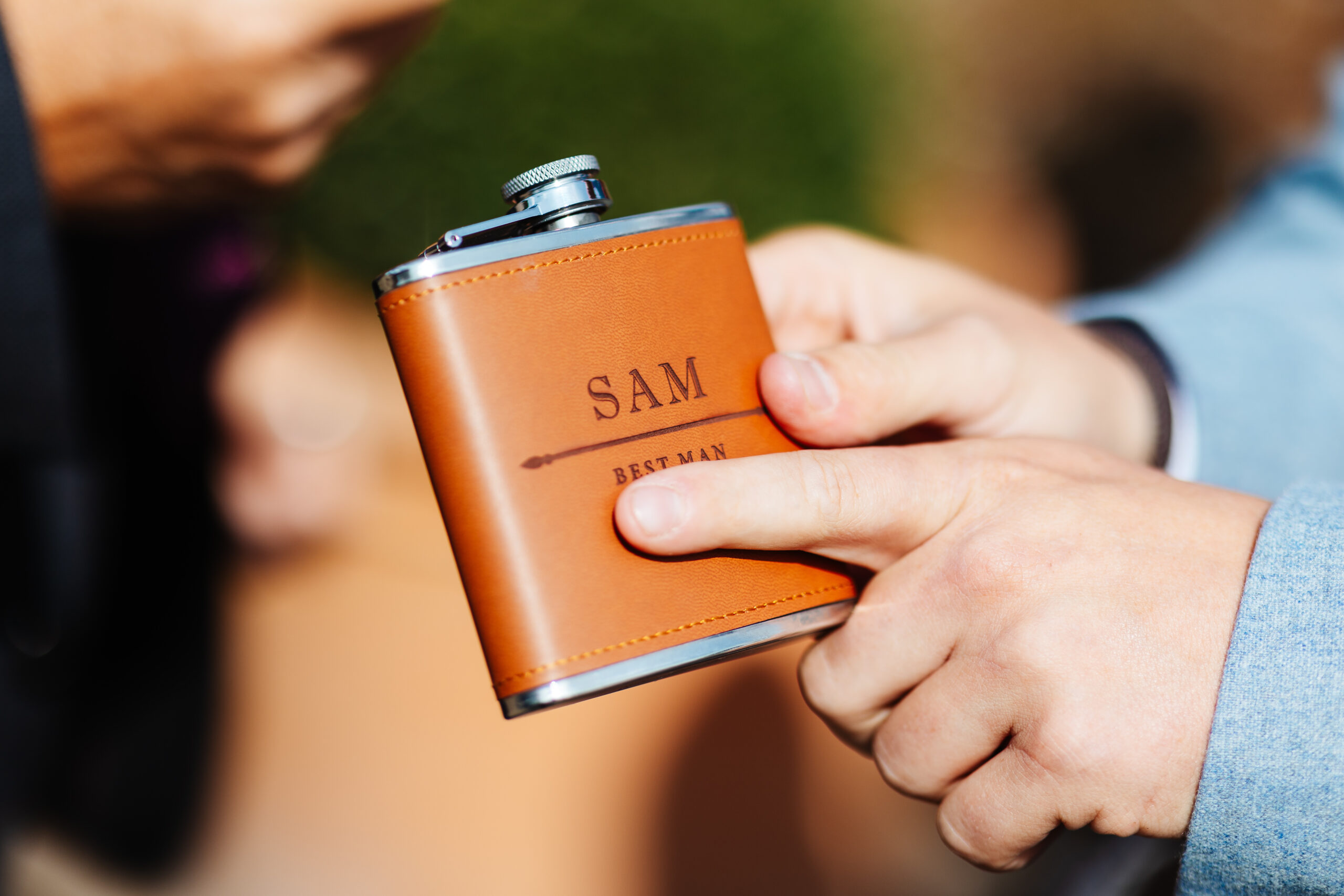 A personalised, brown leather hip flask. It has Sam written on it and best man.