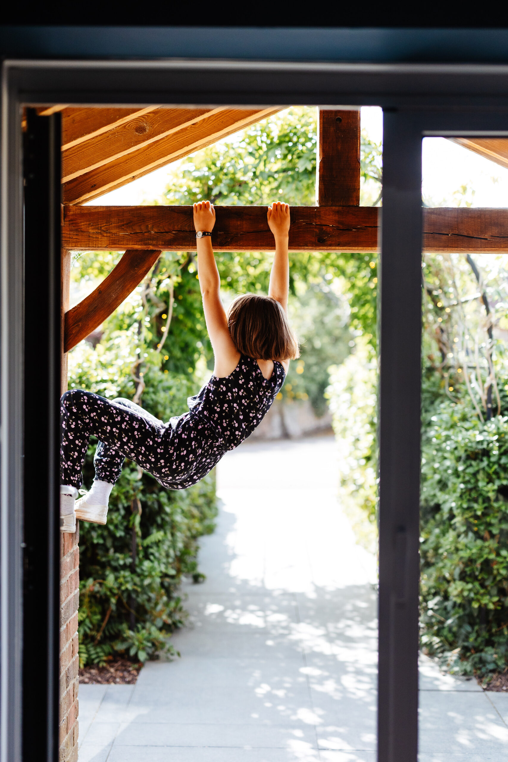 A little girl wearing a black playsuit. She is hanging from the beams.