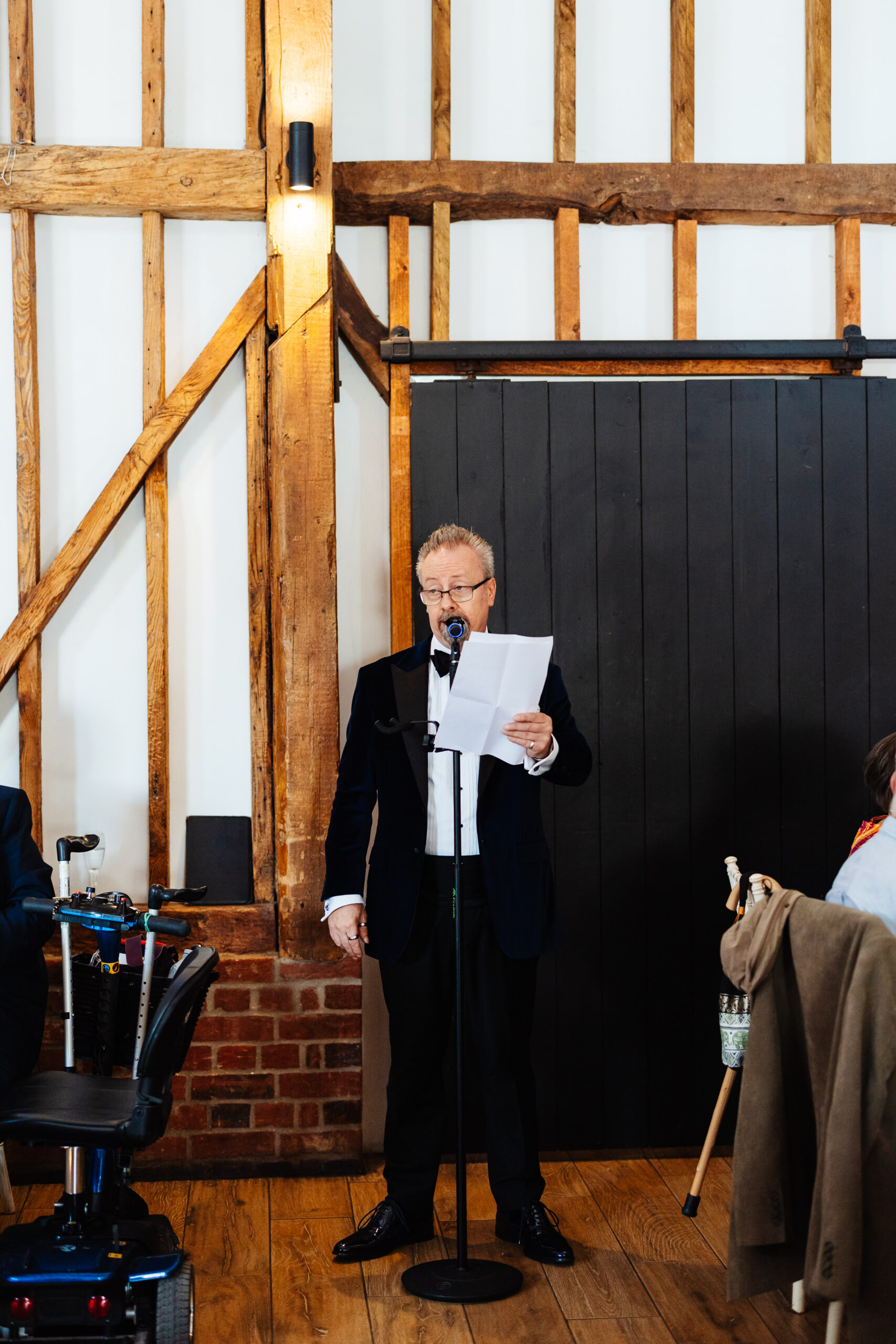 The father of the bride in front of a microphone. He is holding a piece of paper and is reading his speech.