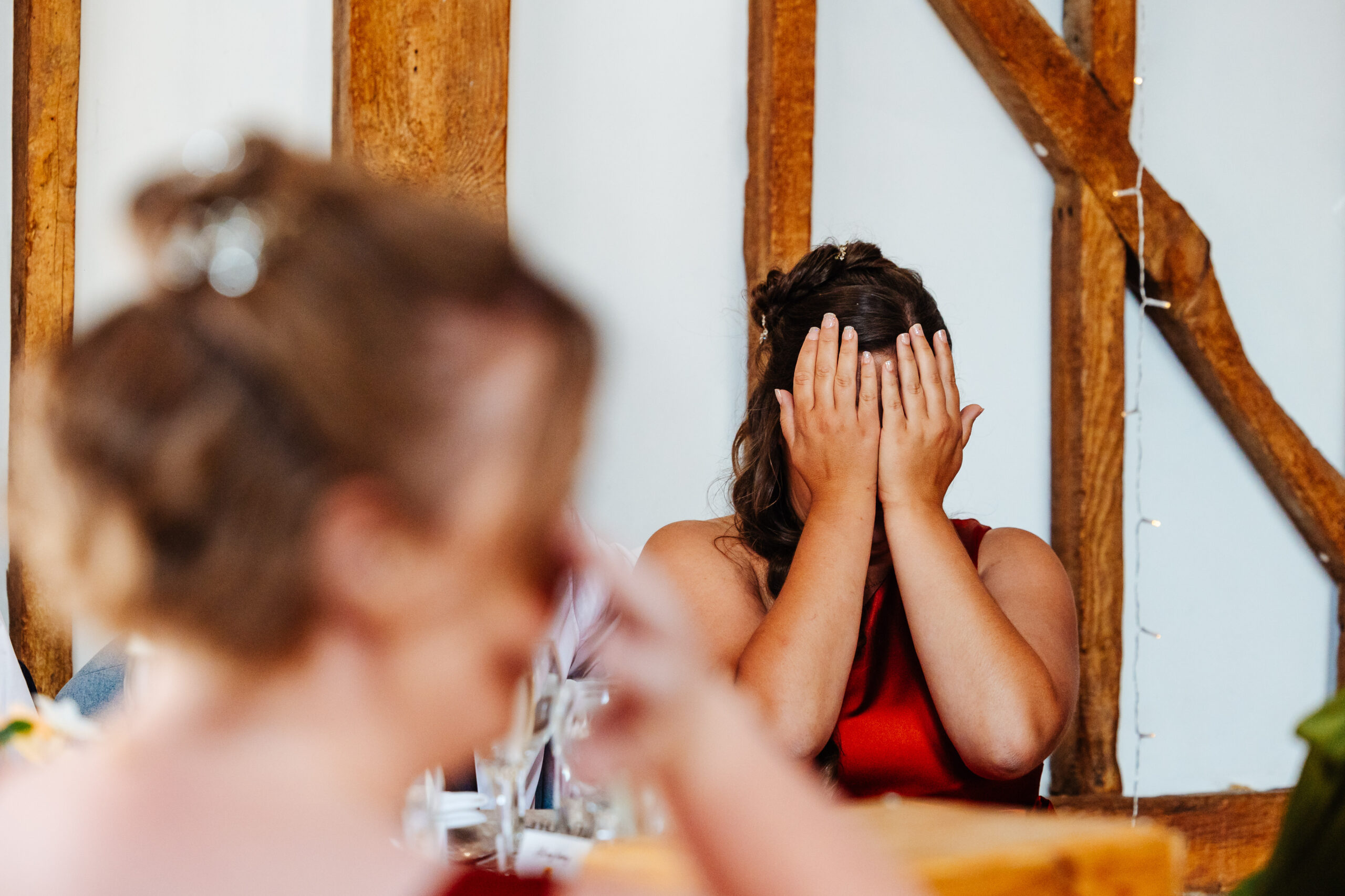 A guest sat down at a table. She has both hands over her face in embarrassment during the speeches.