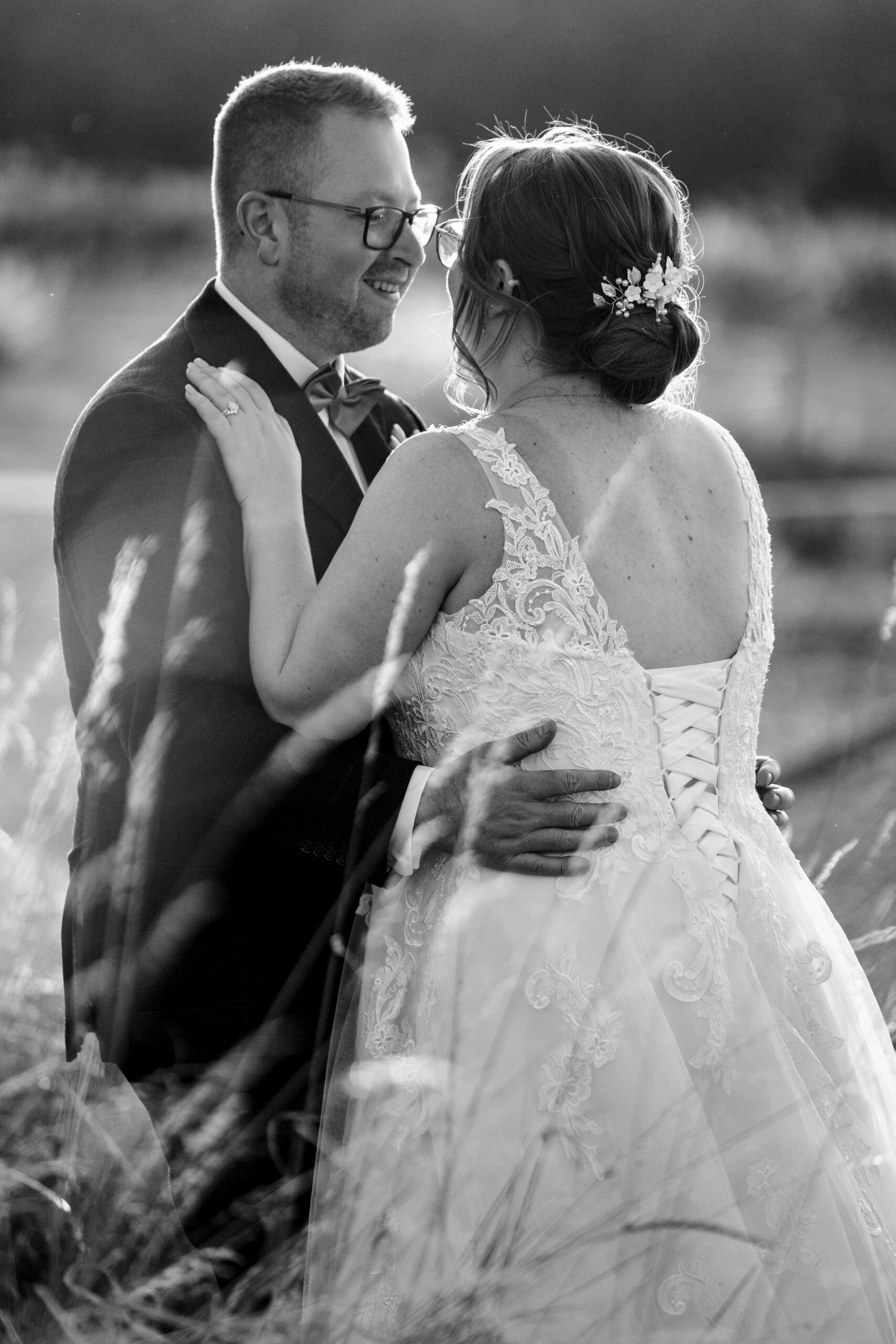 A black and white image of the bride and groom. They are holding each other and smiling. They are in a corn field.