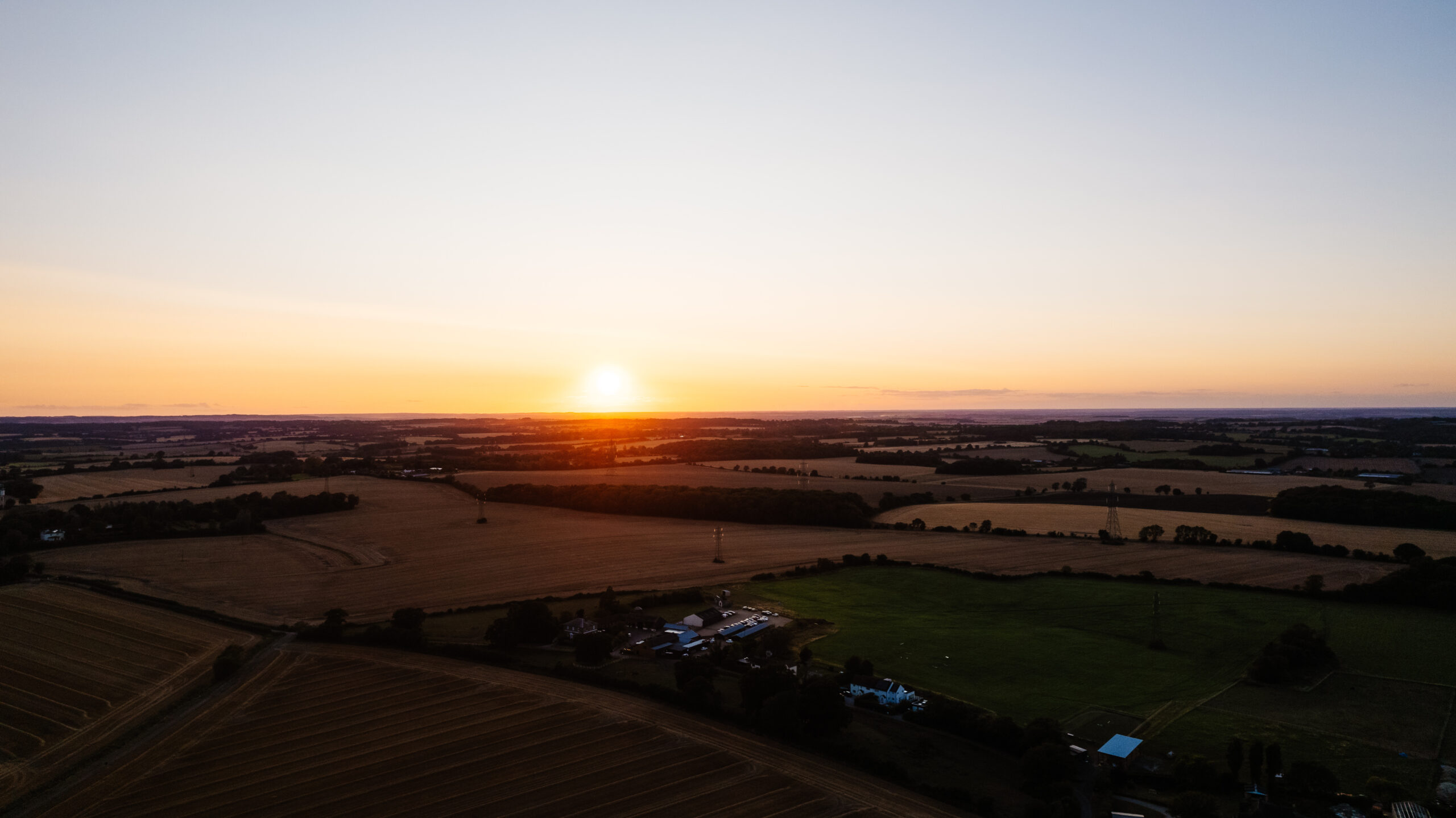 A photo of the sun setting over the venue. It is a drone shot and you can see fields around it.