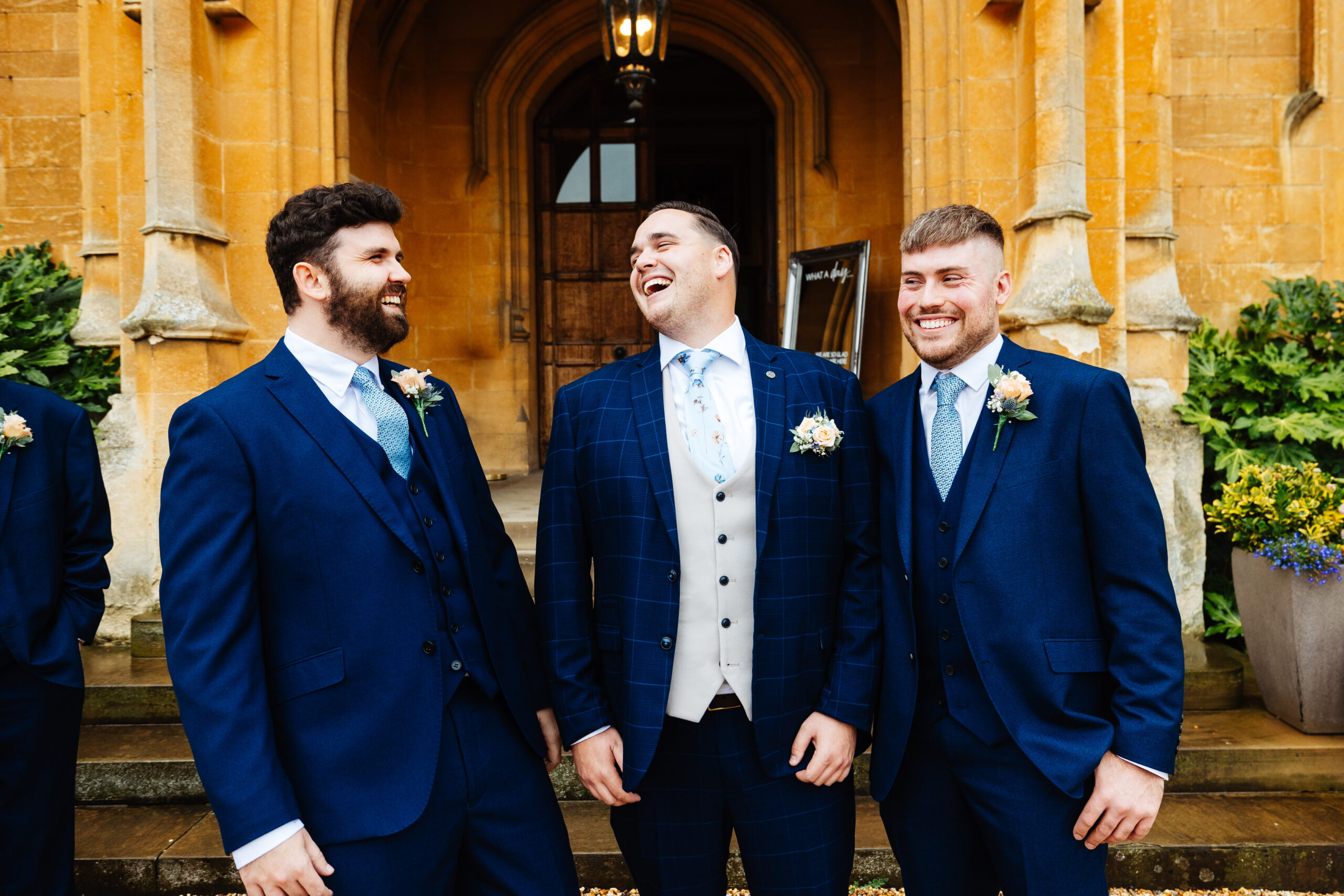 The groom and his groomsmen outside Shuttleworth House. They are all in navy blue suits. They are looking at each other and smiling.