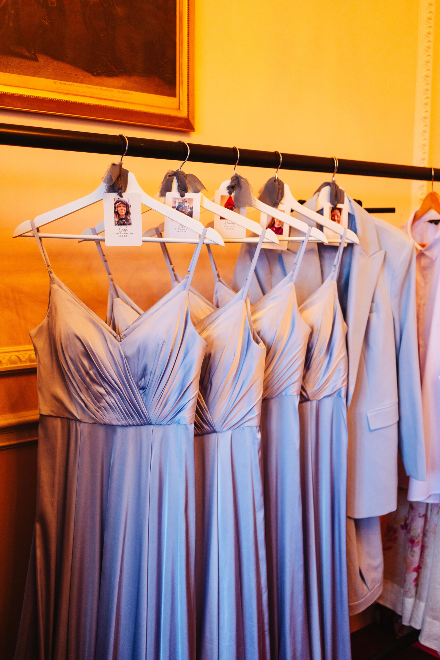 A set of long, lilac dresses hanging up on a rail. There are photos on tags of the coat hanger too.