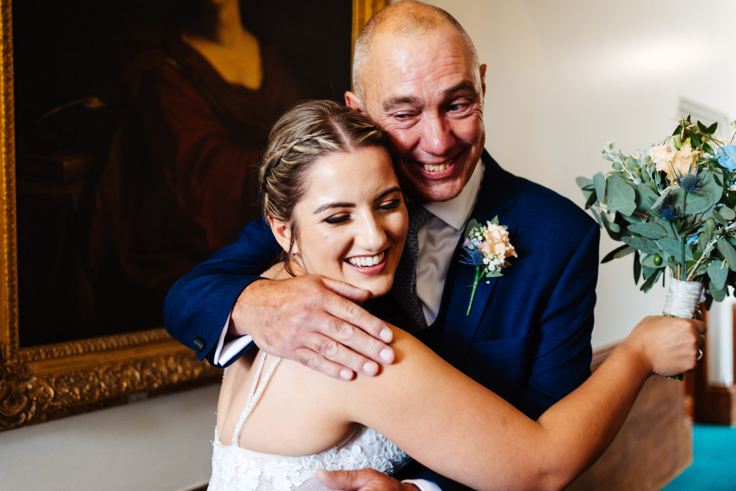 The bride and her father embracing. He is crying and has his arms around her.