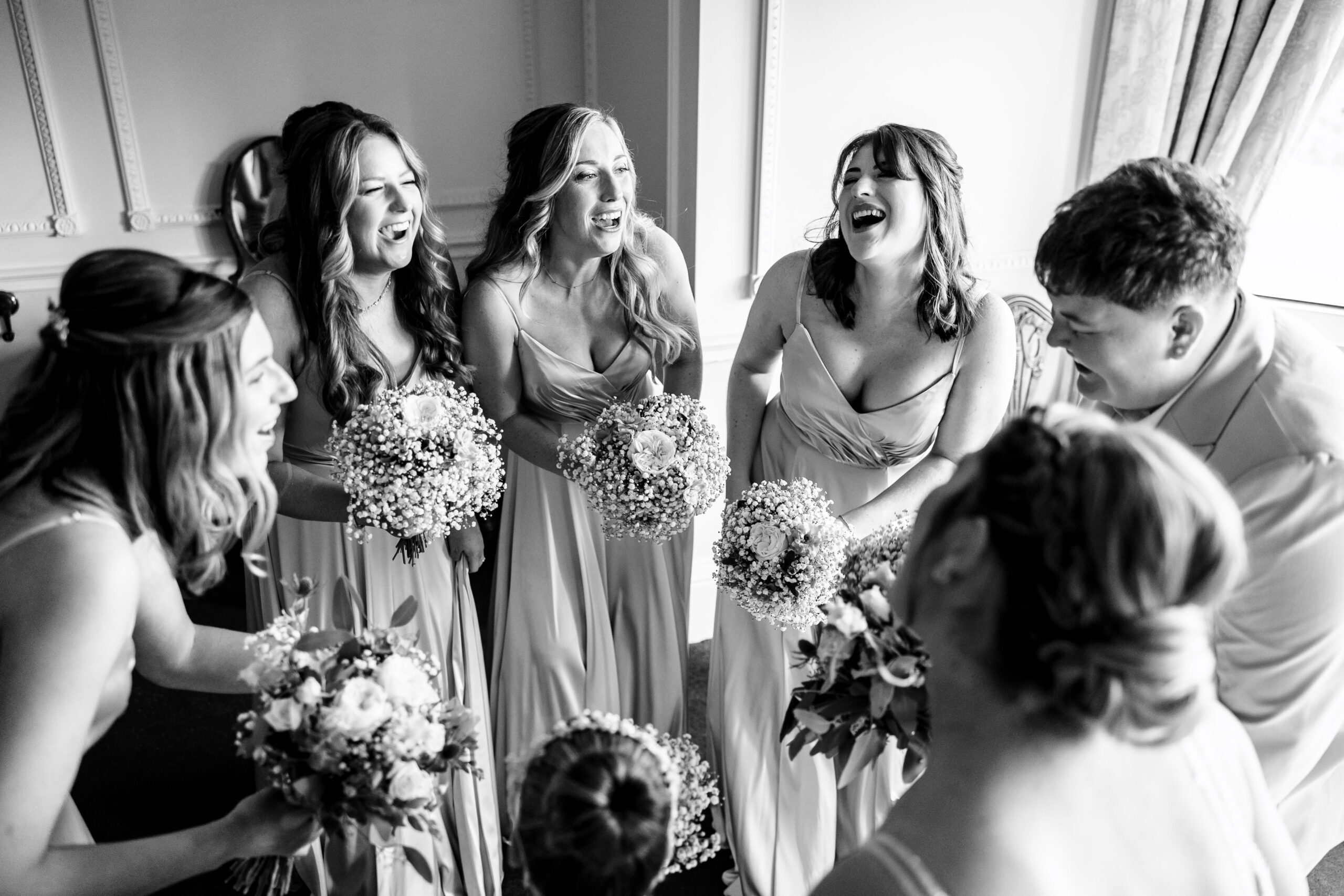 A black and white photo of the bridesmaids and the bride. They are all in a circle and are smiling.