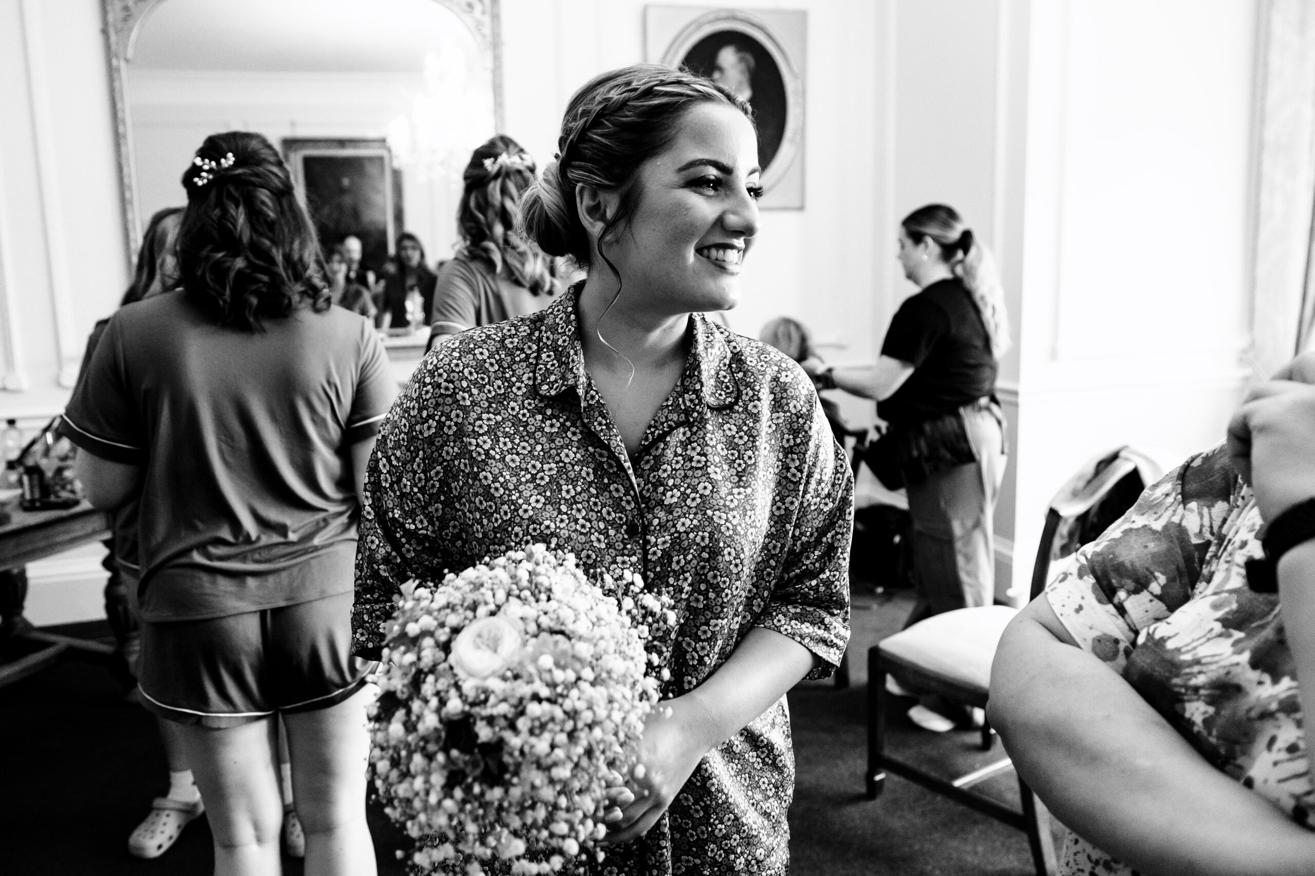 A black and white photo of the bride. She is wearing floral patterned pyjamas and is holding a small bouquet of flowers.