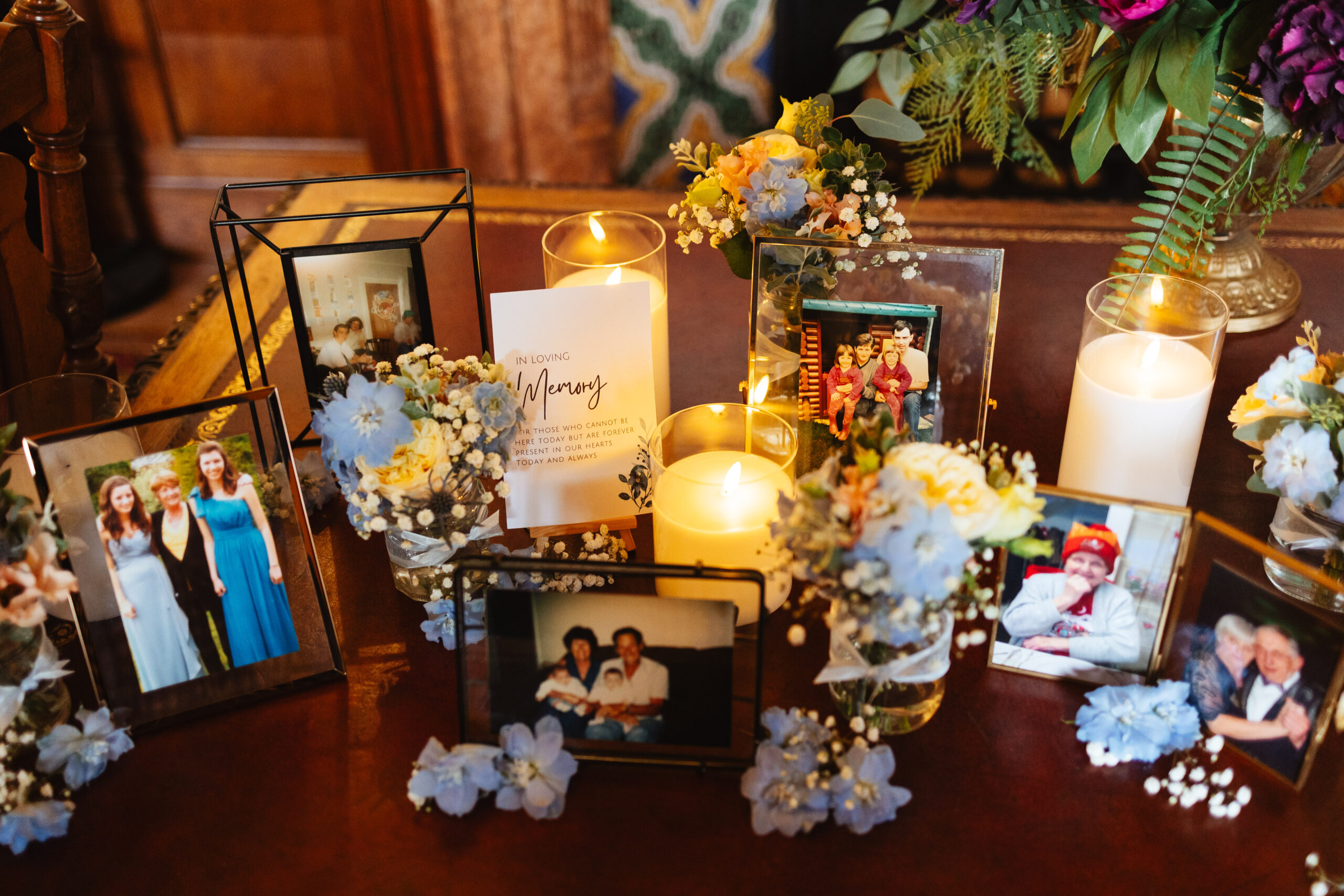 A selection of photographs with "In loving memory" written nearby. They are in lovely frames surrounded by blue flowers and lit candles.