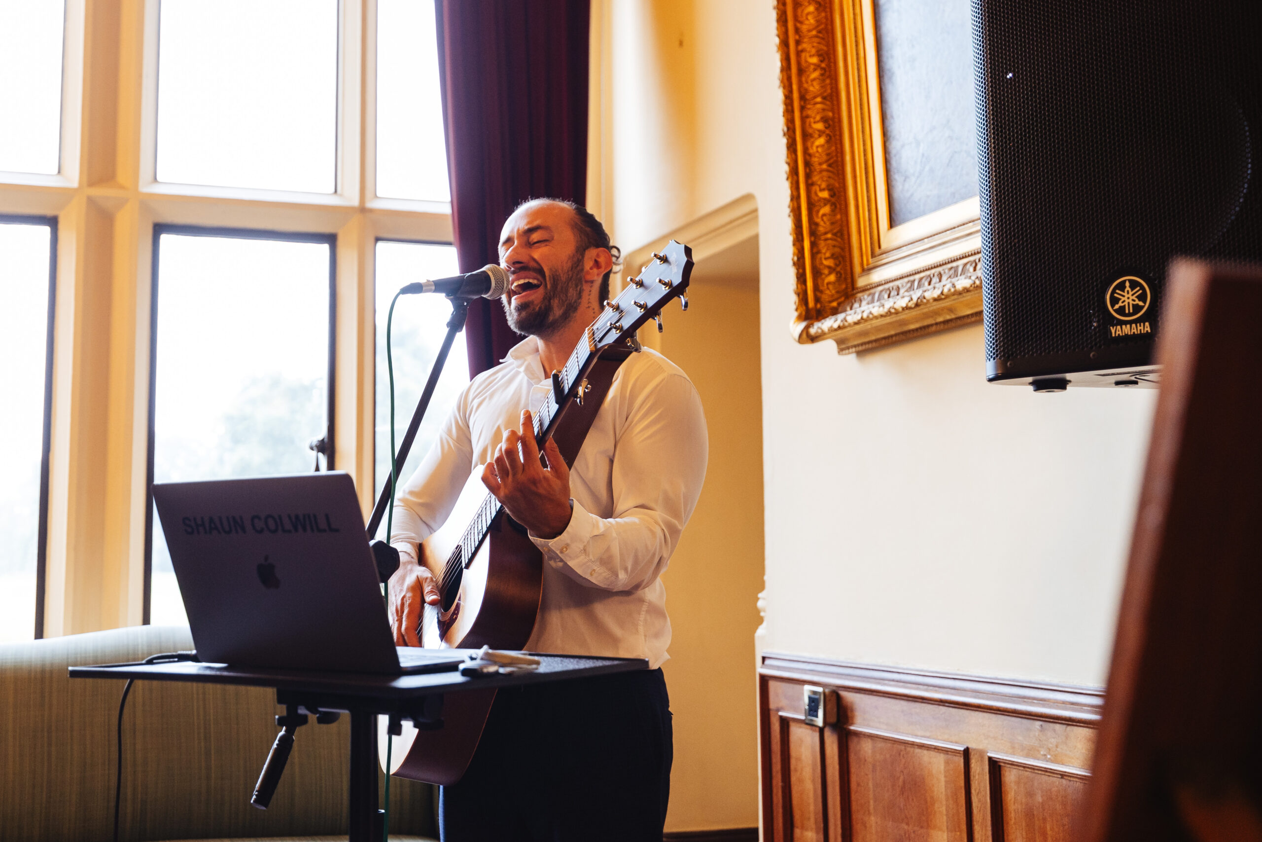 A musician playing a guitar and singing in to a microphone.