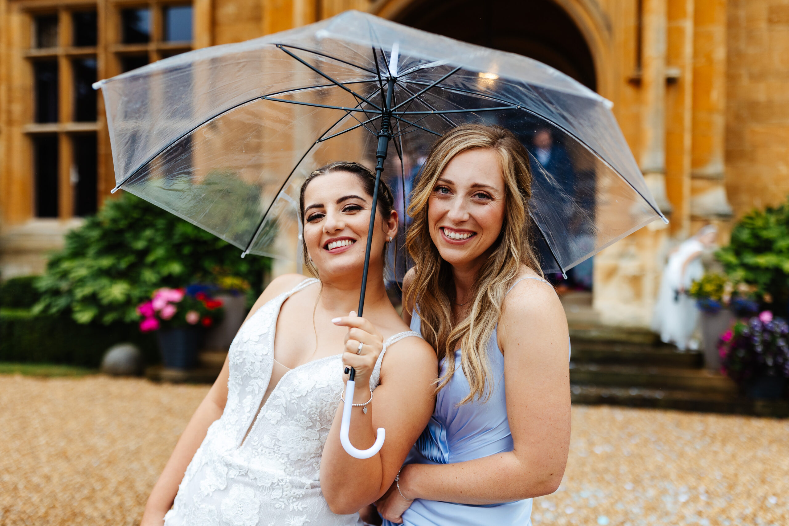 The bride and one of her bridesmaids outside. She is holding an umbrella as it is raining slightly.