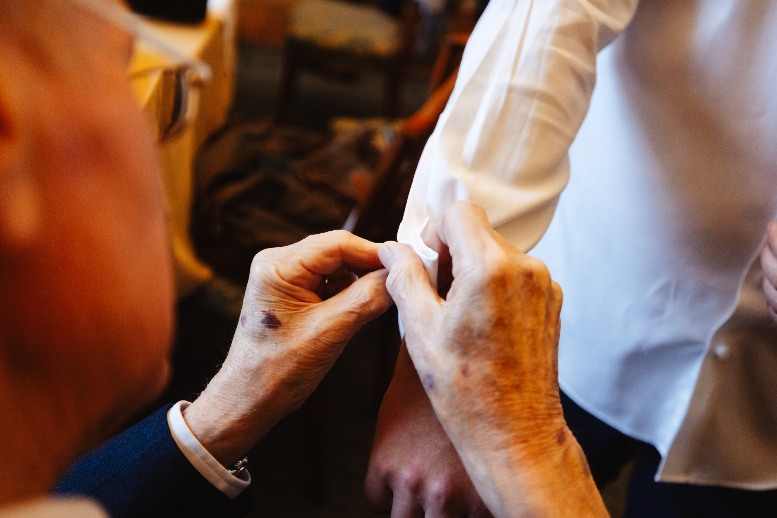 A pair of older hands putting a cuff link on the groom.