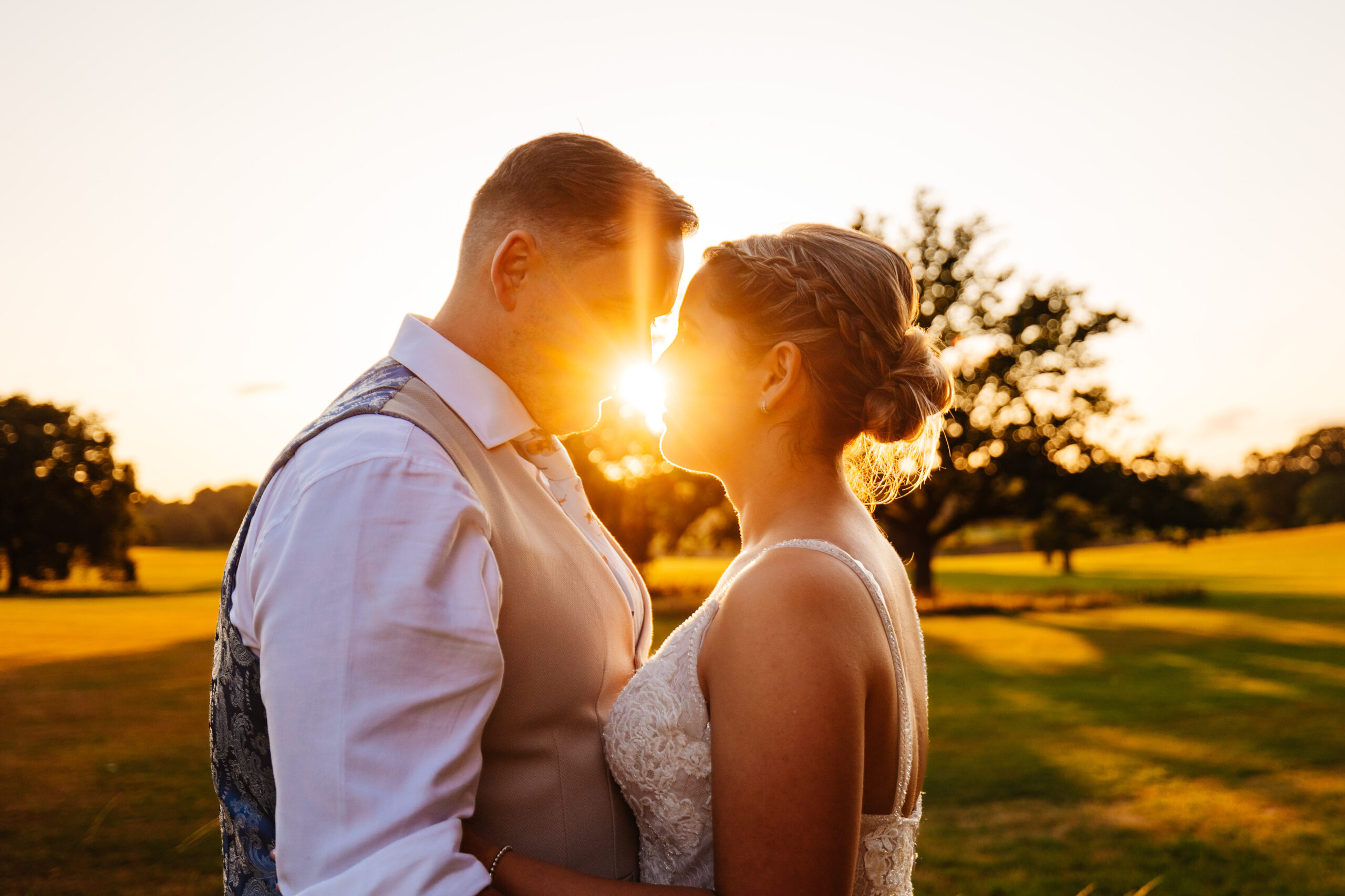 A photo of the bride and groom. The sunlight is between them. They are close and embracing one another.