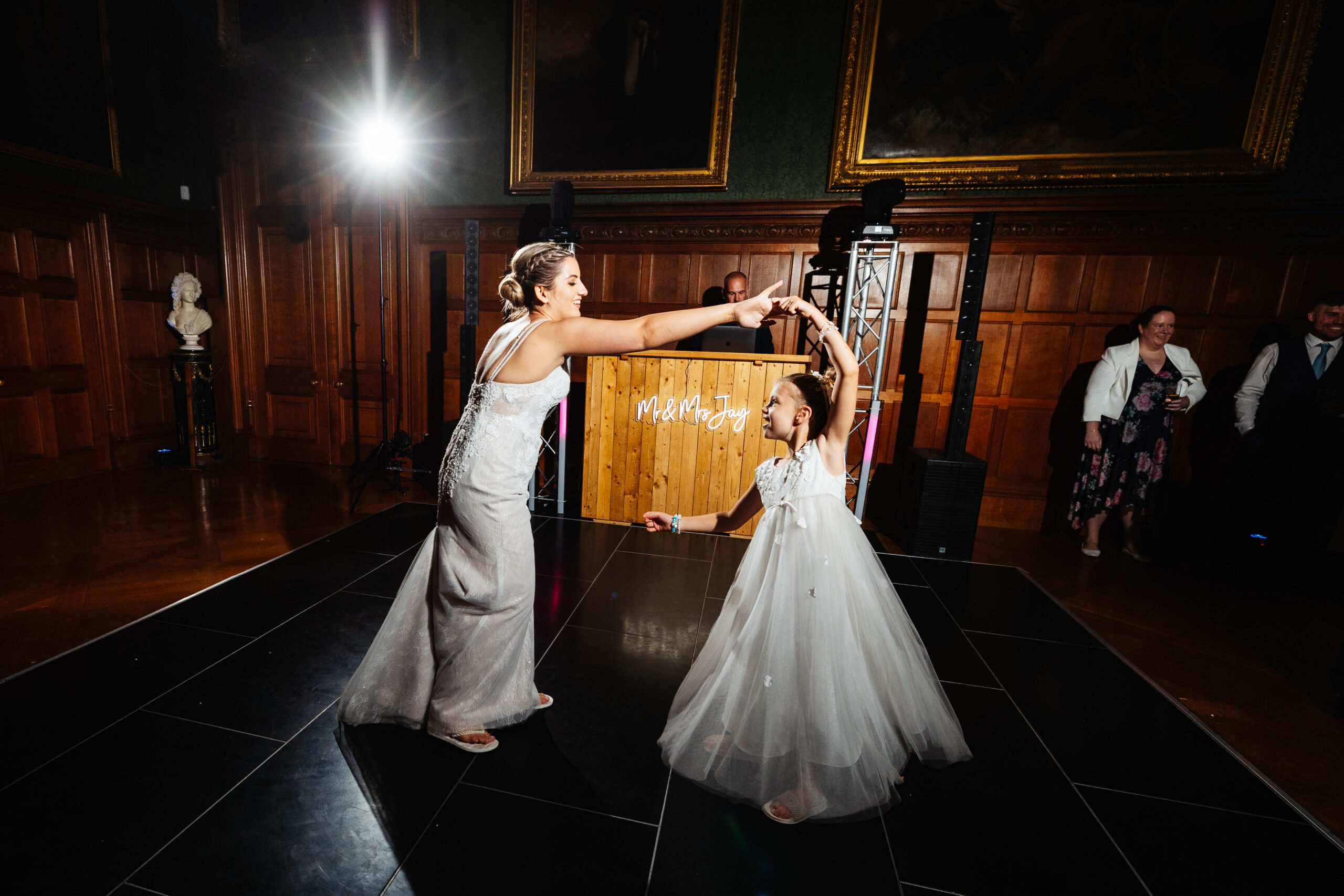 The bride on the dance floor twirling her little flower girl around. They are looking at each other and the little girl is smiling.