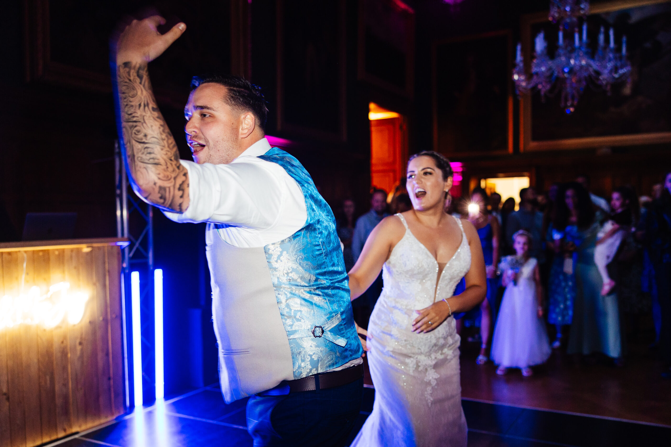 The bride and groom on the dancefloor. The groom has his hand in the air welcoming others on to the floor.