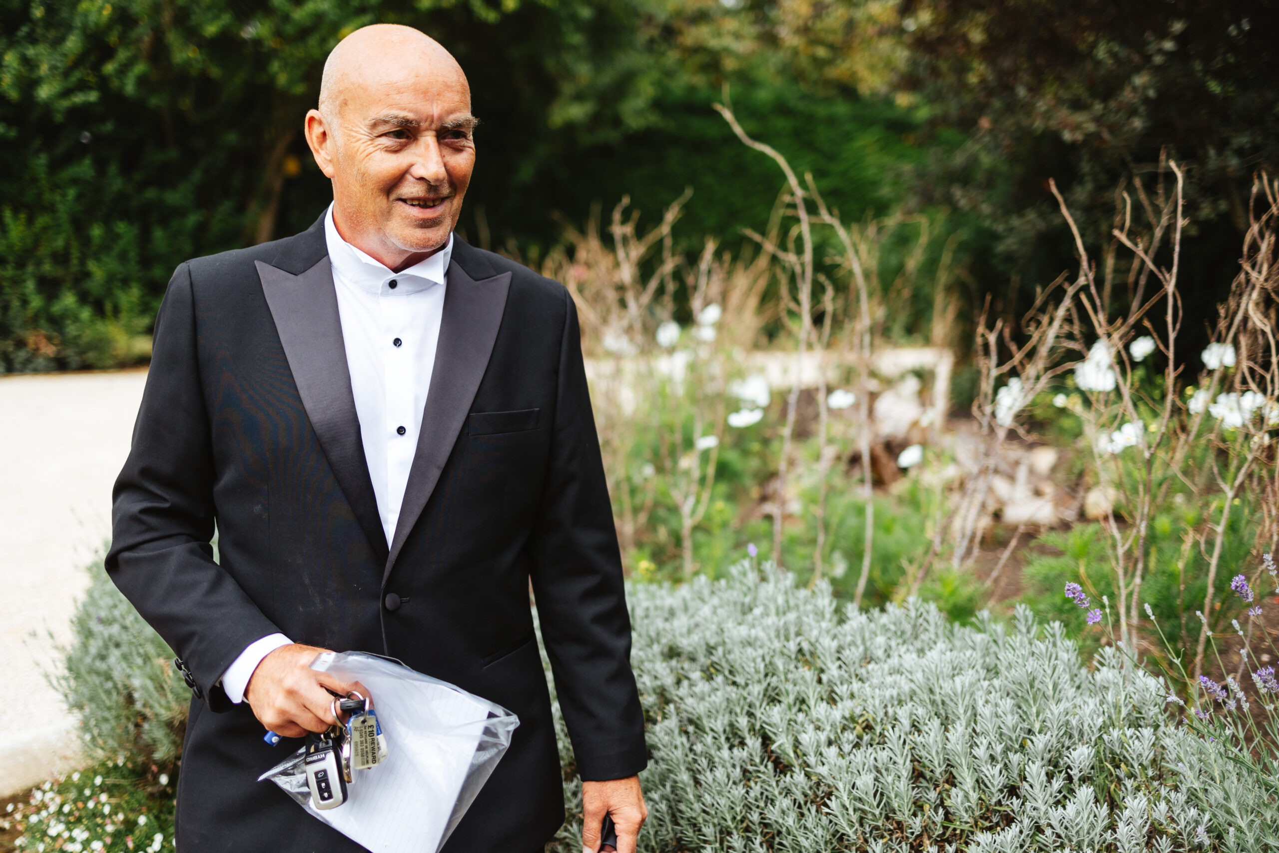 The father of the bride in the gardens. He is wearing a black tux.