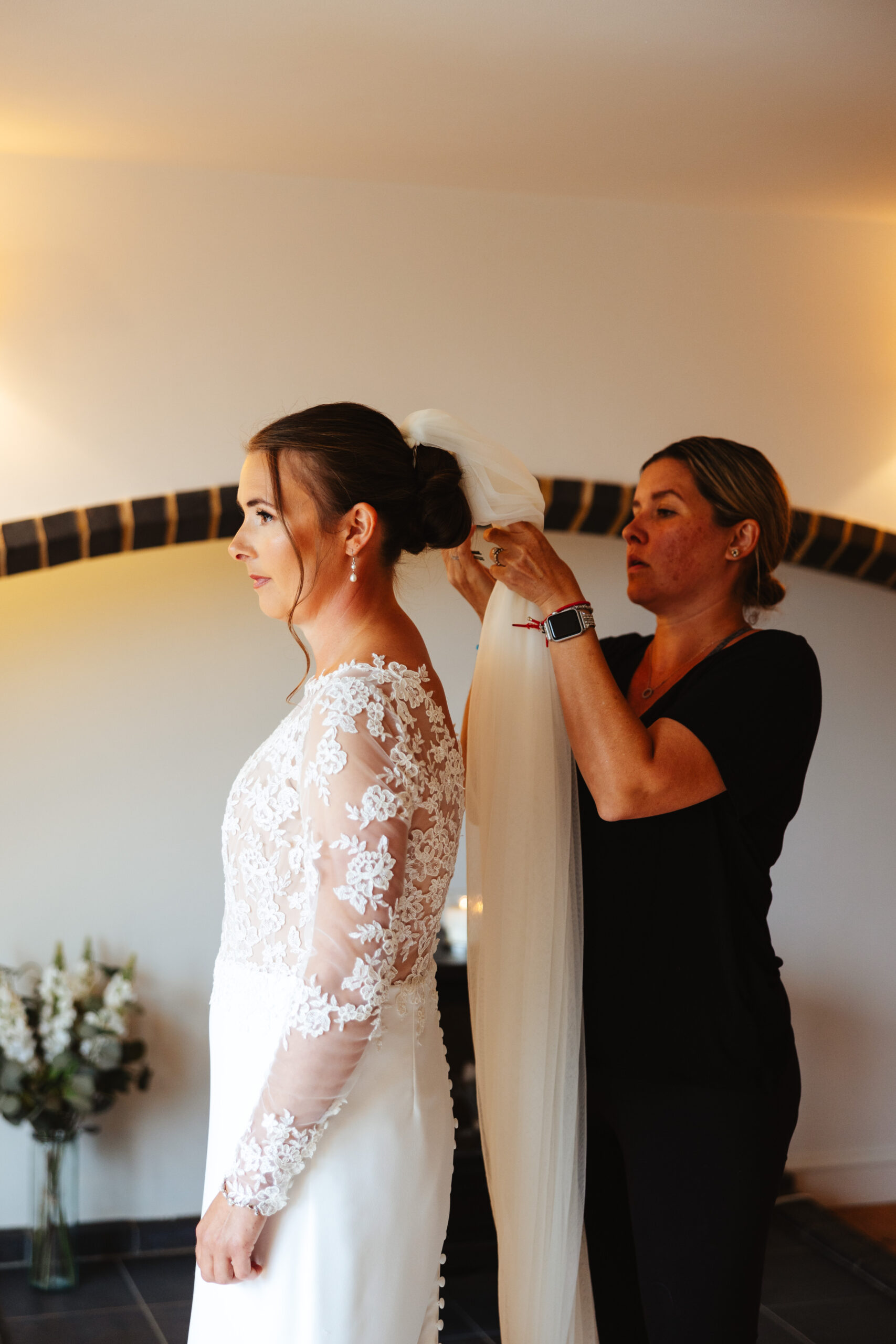 The hairdresser putting in the bride's veil in to her hair. The bride is looking away from the camera and she looks nervous.