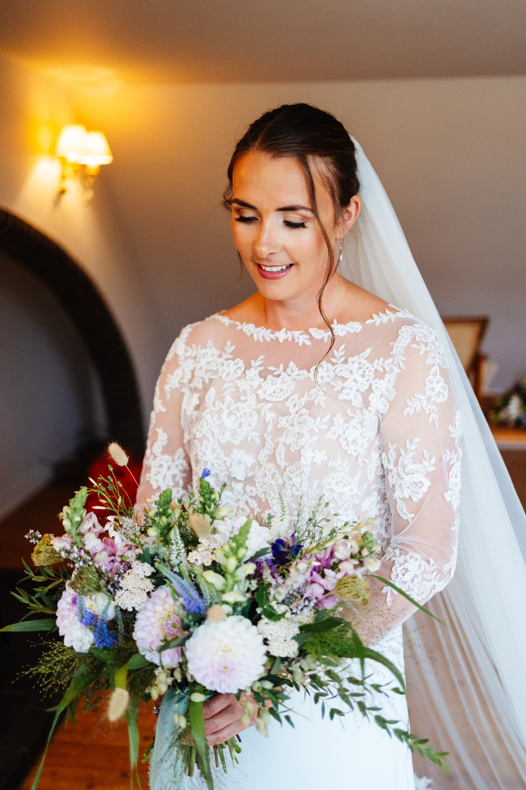 The bride in her dress and holding her bouquet. The flowers are a mixture of pinks, purples, blues and white.