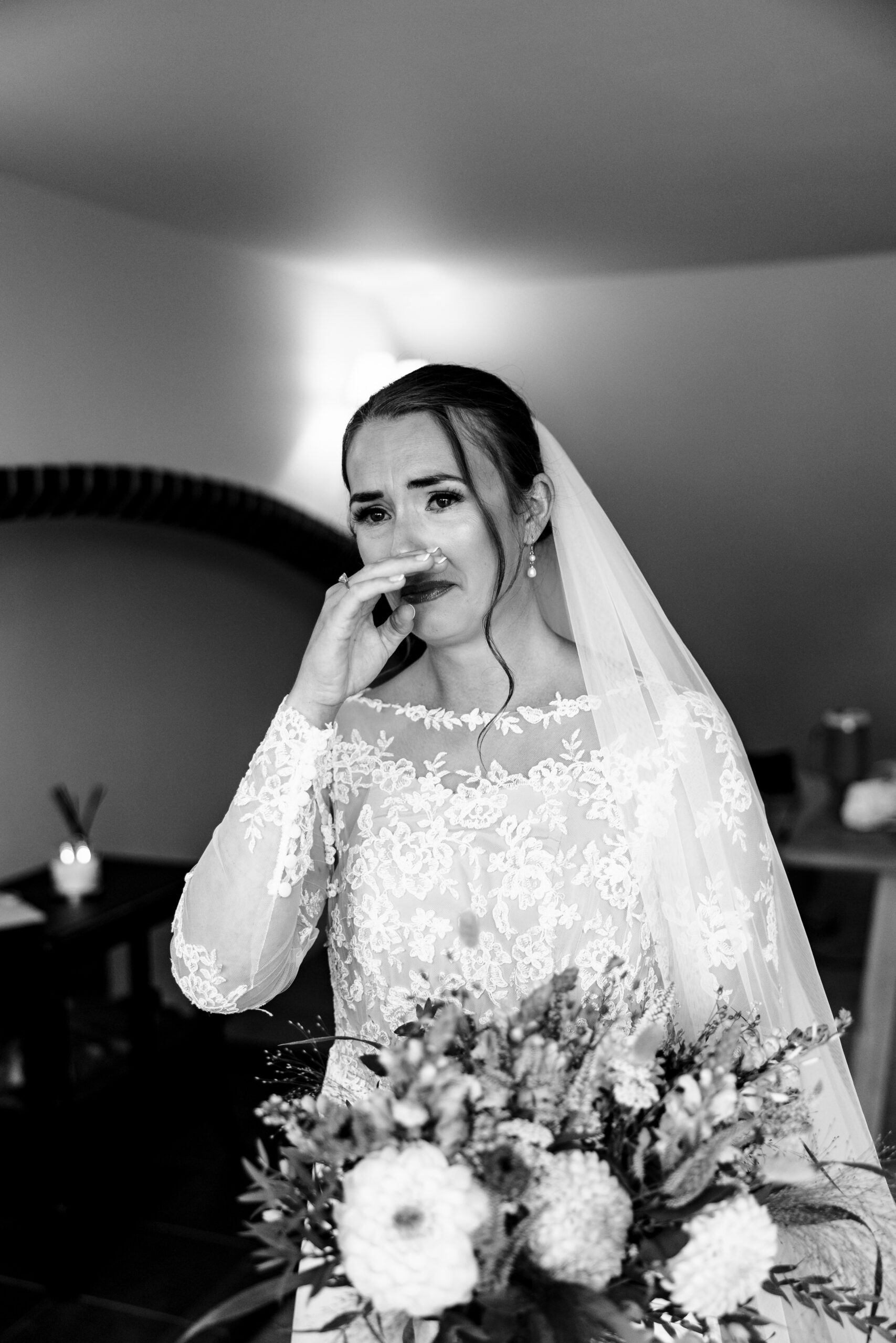 The bride looking very emotional. She has her hand raised to her face and is crying.